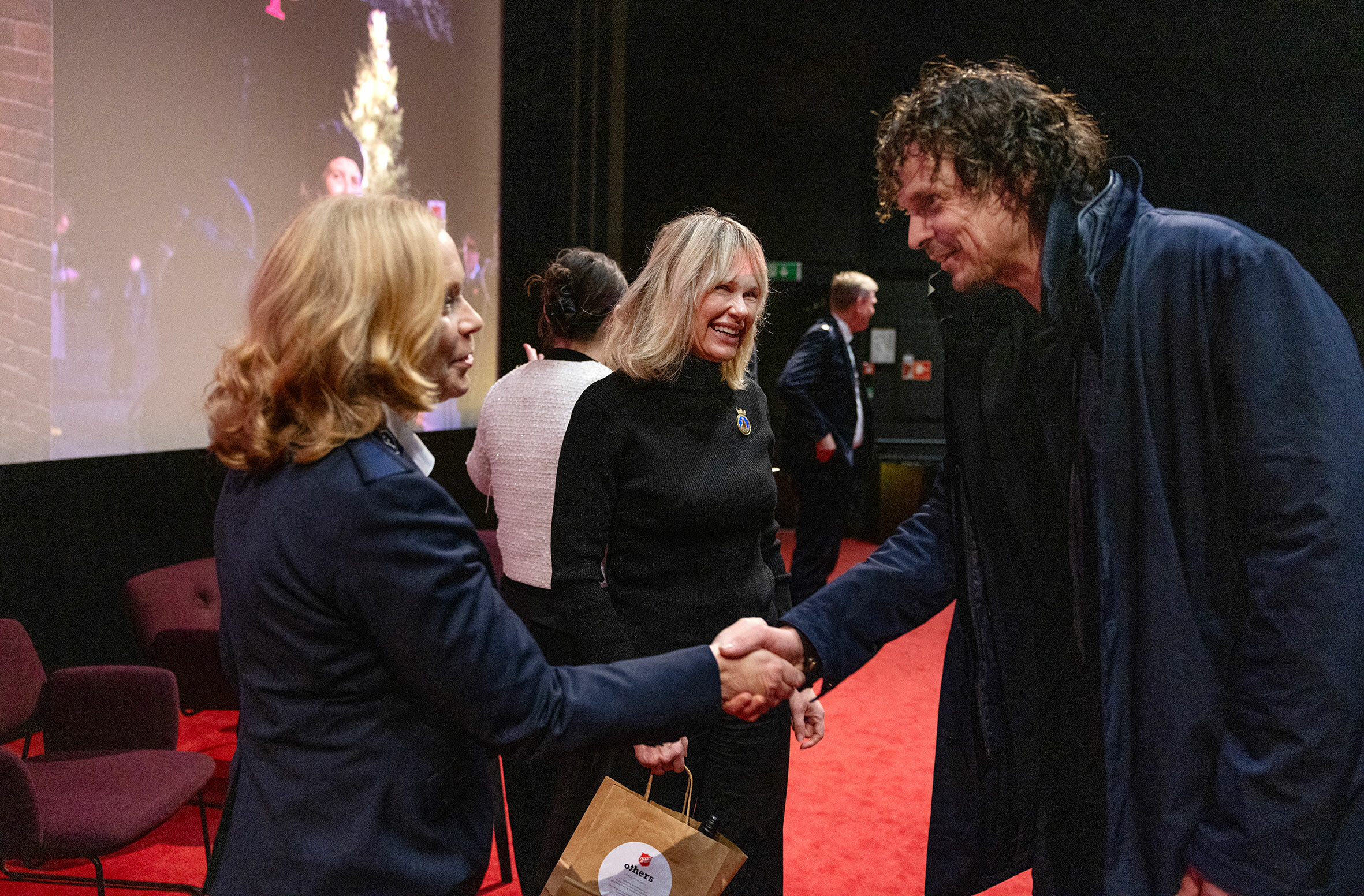 Kvinne og mann håndhilser i en kinosal. I bakgrunnen, mellom dem, står en smilende kvinne.