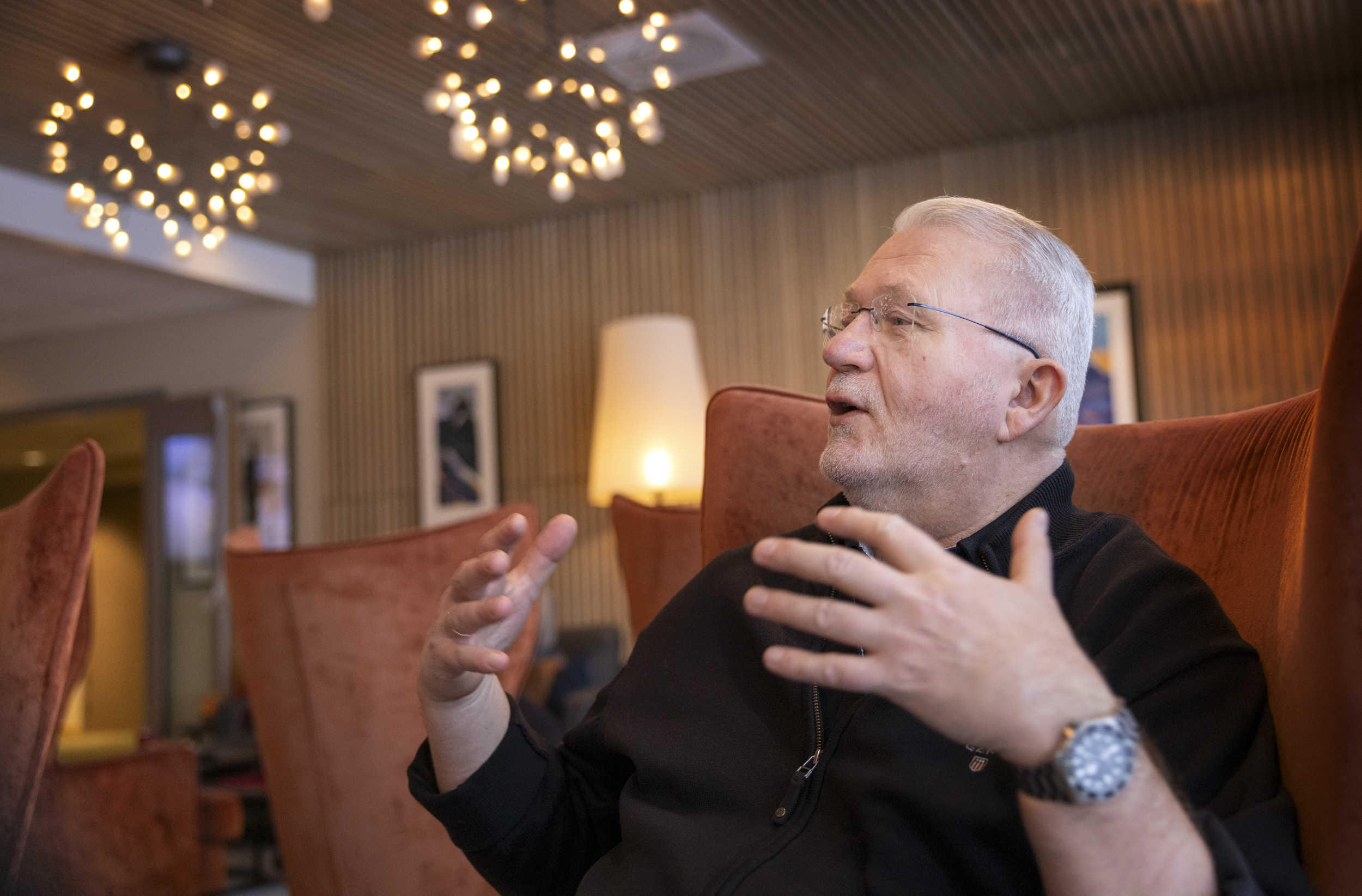 Mann som sitter i en lenestol i en hotellobby. Gestikulerer med hendene.