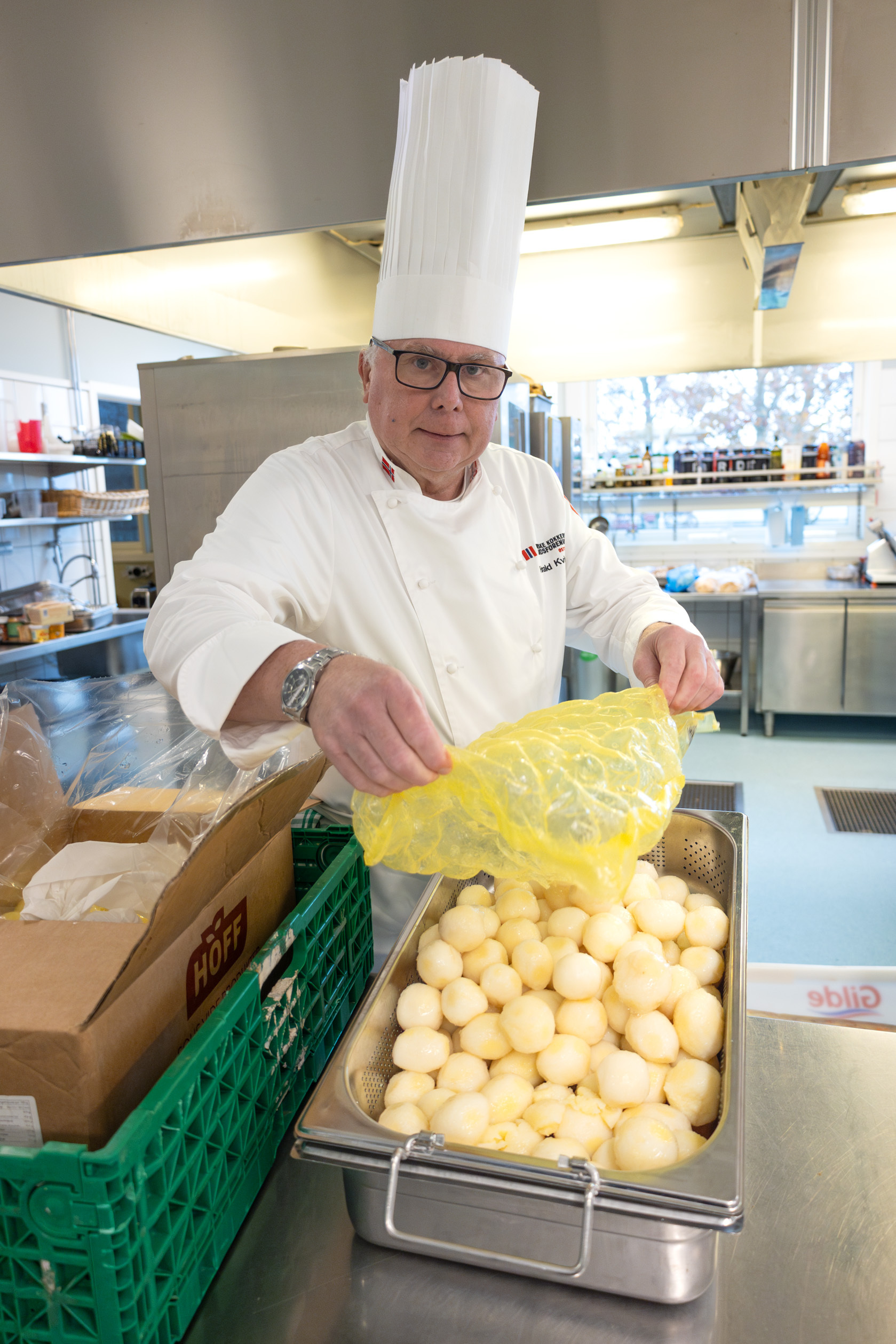 Foto: Mann i hvit kokkeuniform med høy hatt heller vakumpakkede poteter i en stor aluminiumsform.