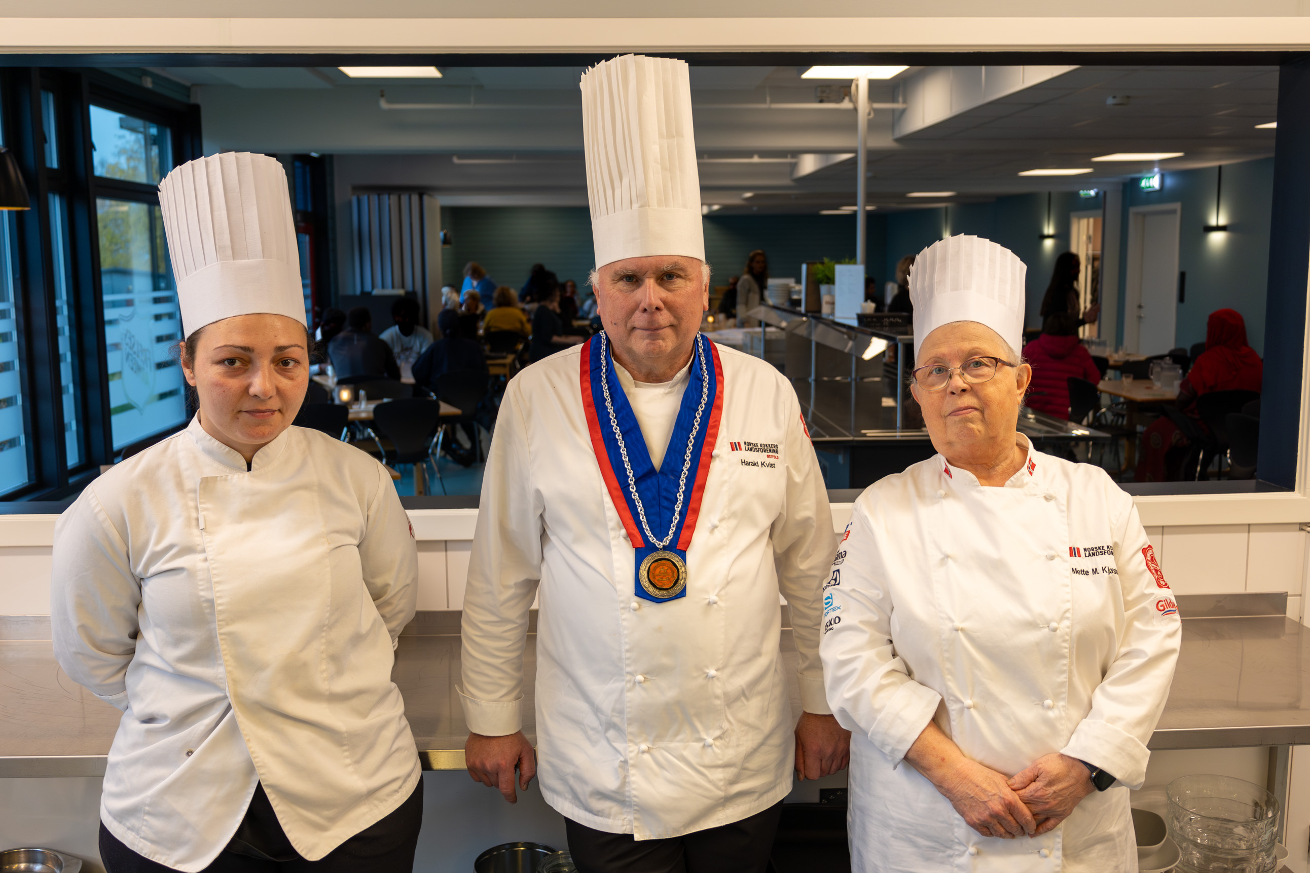 Foto: Tre kokker står oppstilt foran serveringsluka. Mannen står midten.