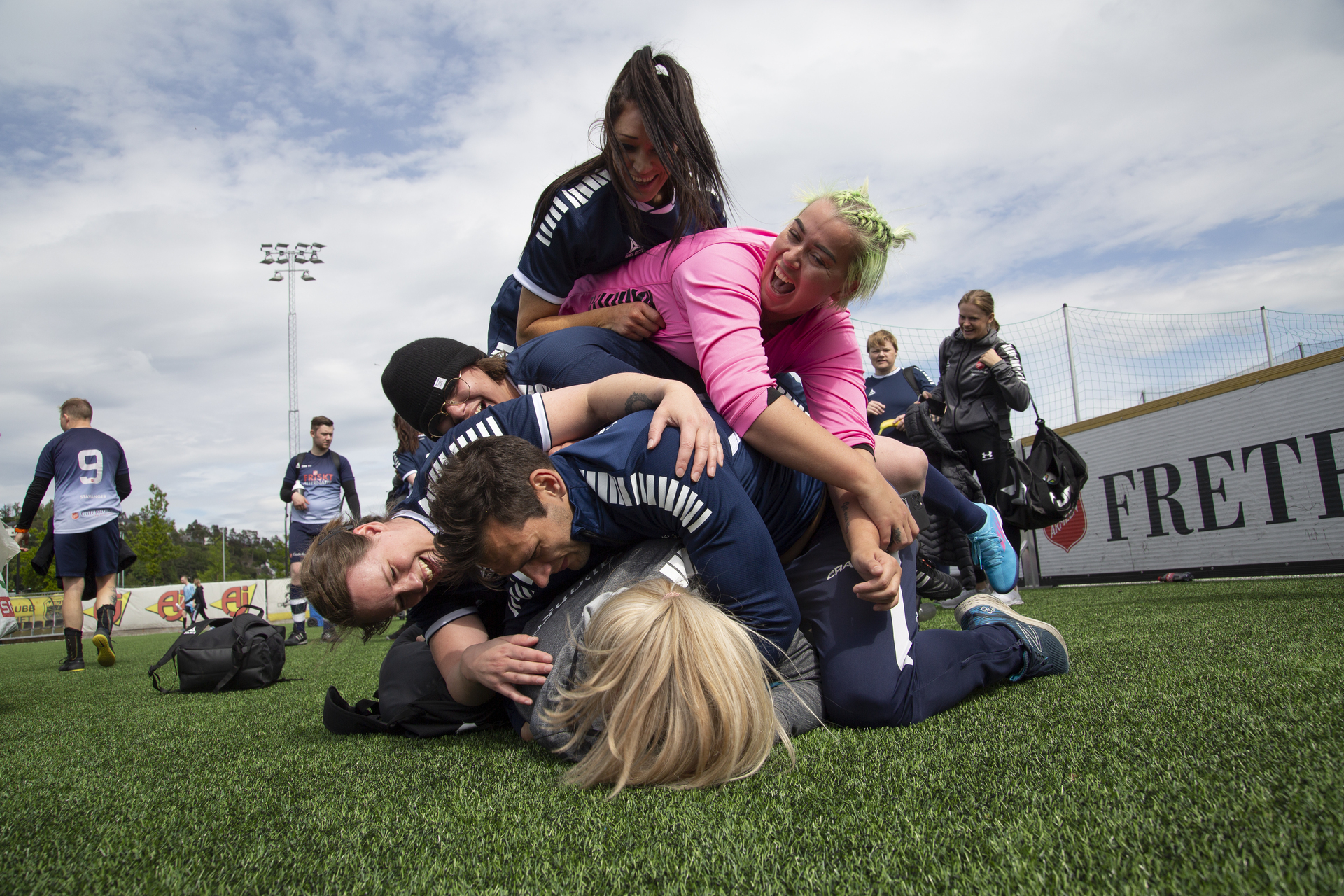 Foto: Fotballspillere av begge kjønn ligger i en stpr røys oppå hverandre etter endt kamp. De ler og har det gøy.