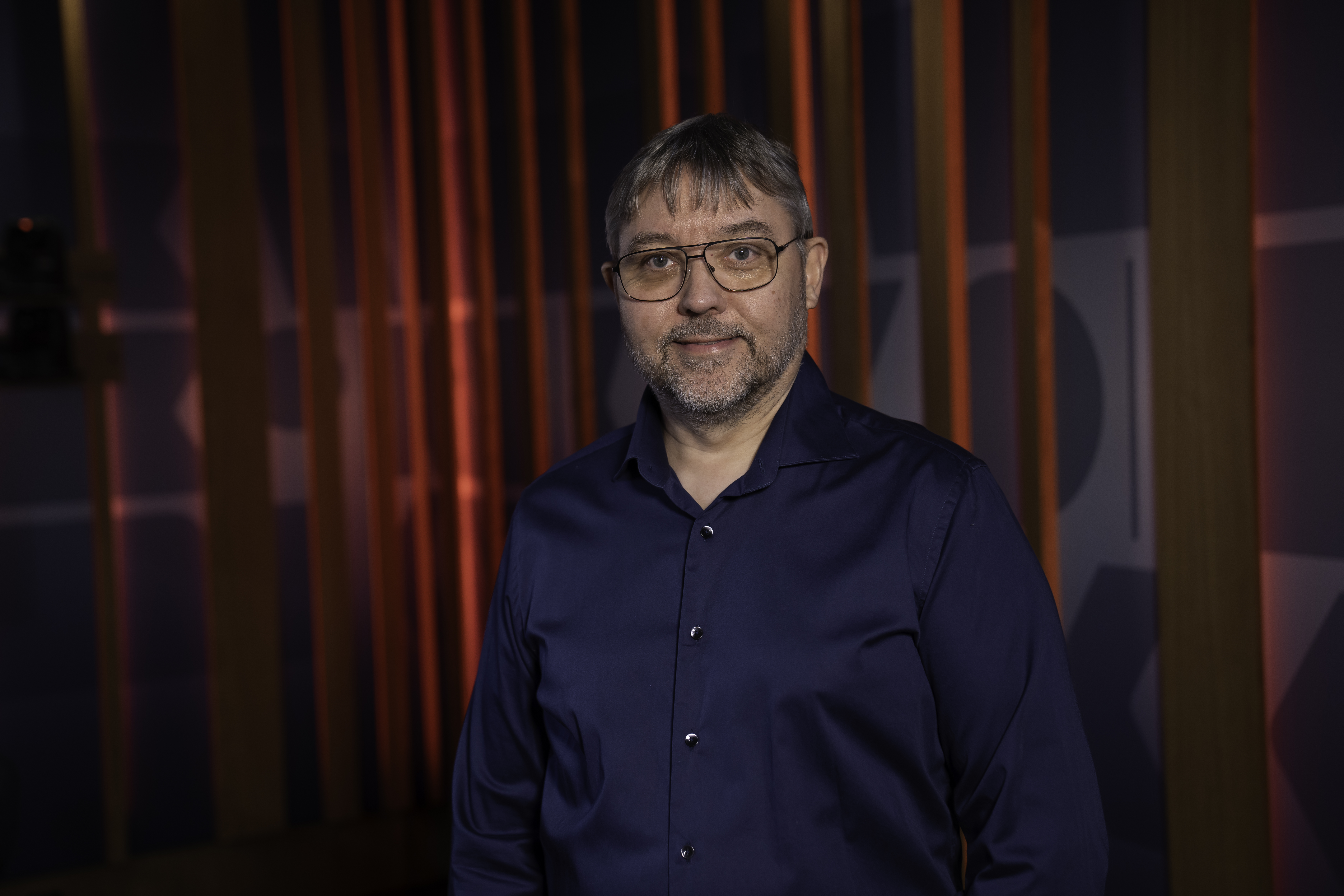 Foto: Mann med briller, mørkeblondt hår og blå skjorte står foran ent rødt sceneteppe.