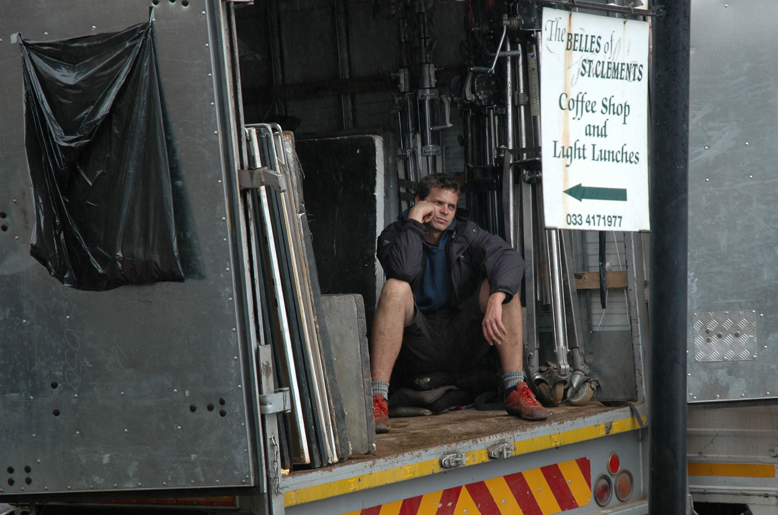 Lastebil med utstyr inni. Begge dørene bak er åpne og inni sitter det en ung mann.