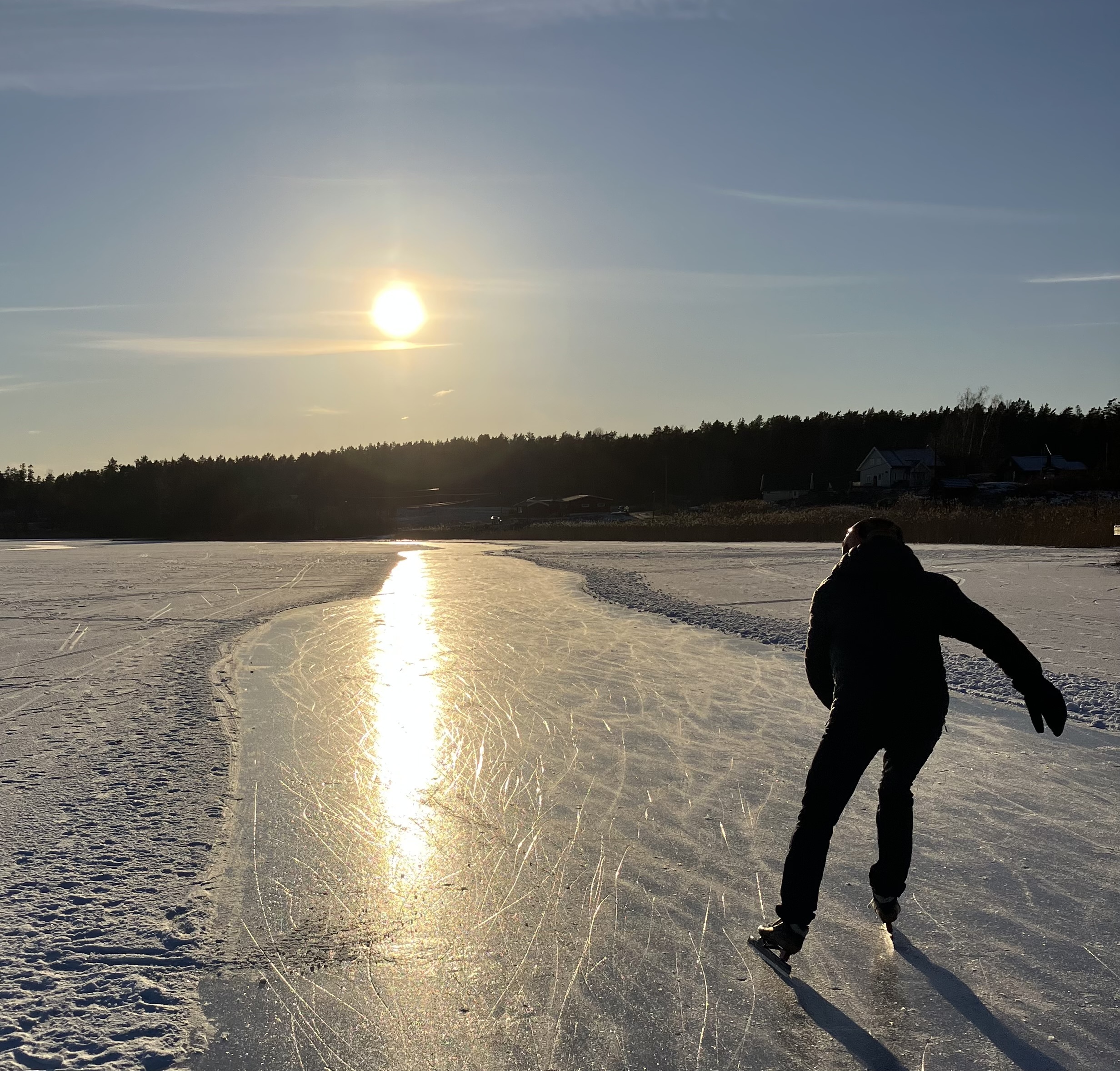 Foto: Silhuetten av en person på skøyter mot sola. Det skinner i isen. Vi ser ryggen på ham ute i høyre kant av bildet.