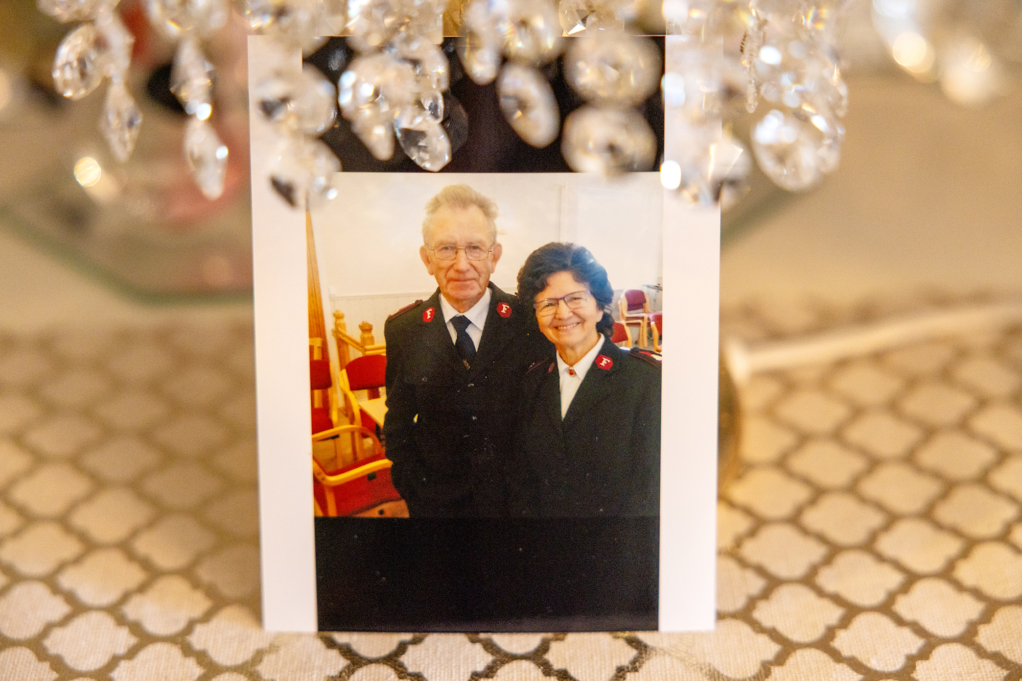 Foto: Bilde av et fotografi, som viser en mann og en kvinne i Frelsesarme-uniformer som smiler mot kamaeraet. Bildet er satt opp på en duk og det henger glasspynt uskarpt i forgrunnen.