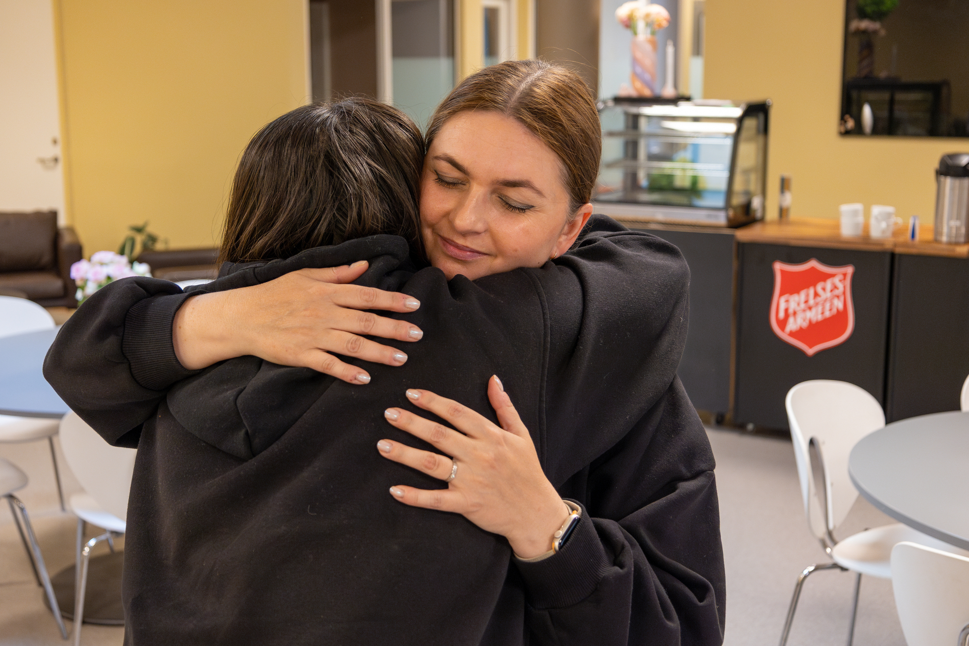 Foto: Kvinne i Frelsesarmeen med mørkt hår og svart genser klemmer en kvinne som også er iført svarte klær og har mørkt hår.