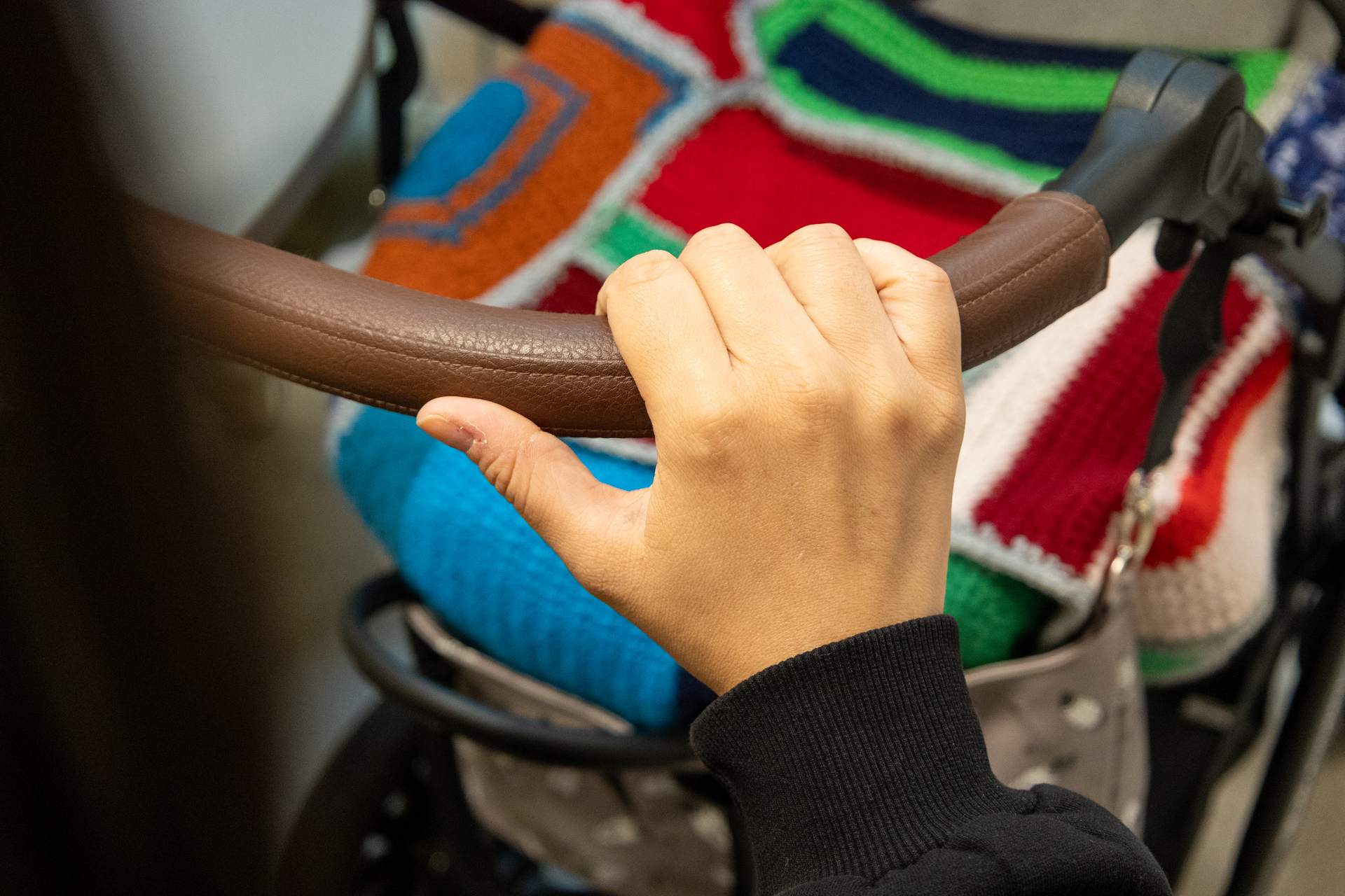 Foto: Hånden til en ung kvinne holder i en barnevogn. Teppet som ligger opp barnet (som vi ikke ser) er et fargerikt lappeteppe.