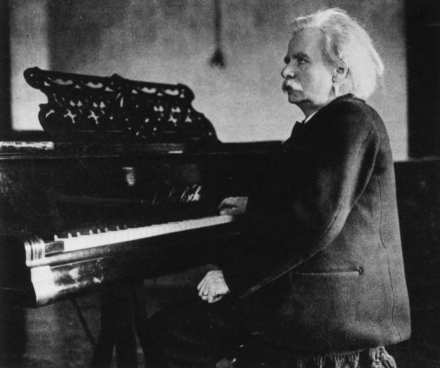 Foto: I svart-hvitt fra 1800-tallet viser en mann med stort, grått hår og bart som sitter dresskledd foran et piano.