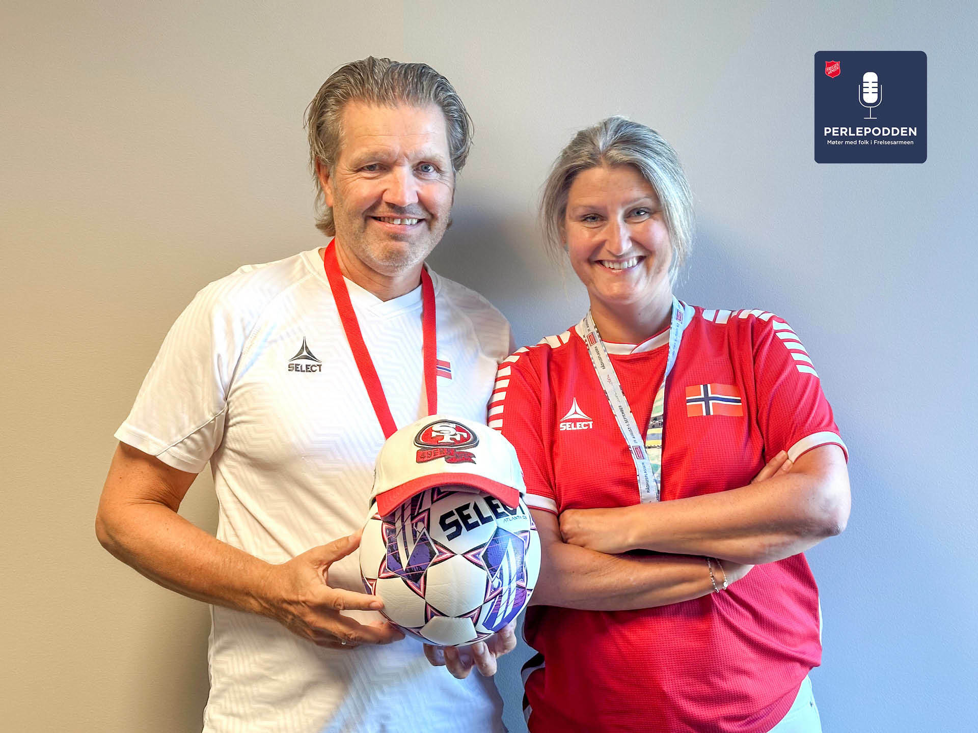 Foto: Mann i hvit trøye og kvinne i rød trøye står tett ved siden av hverandre og smiler. Han holder et fotball som har en caps på hodet. Begge har fløyter hengende i bånd rundt halsen.