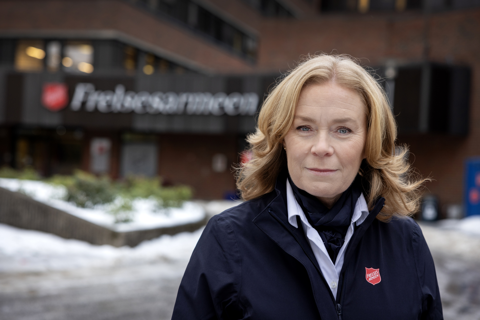 Foto: Kvinne står foran klær Frelsesarmeens hovedkontor med logo synlig over inngangspartiet på bygget. På bakken ligger det snø.