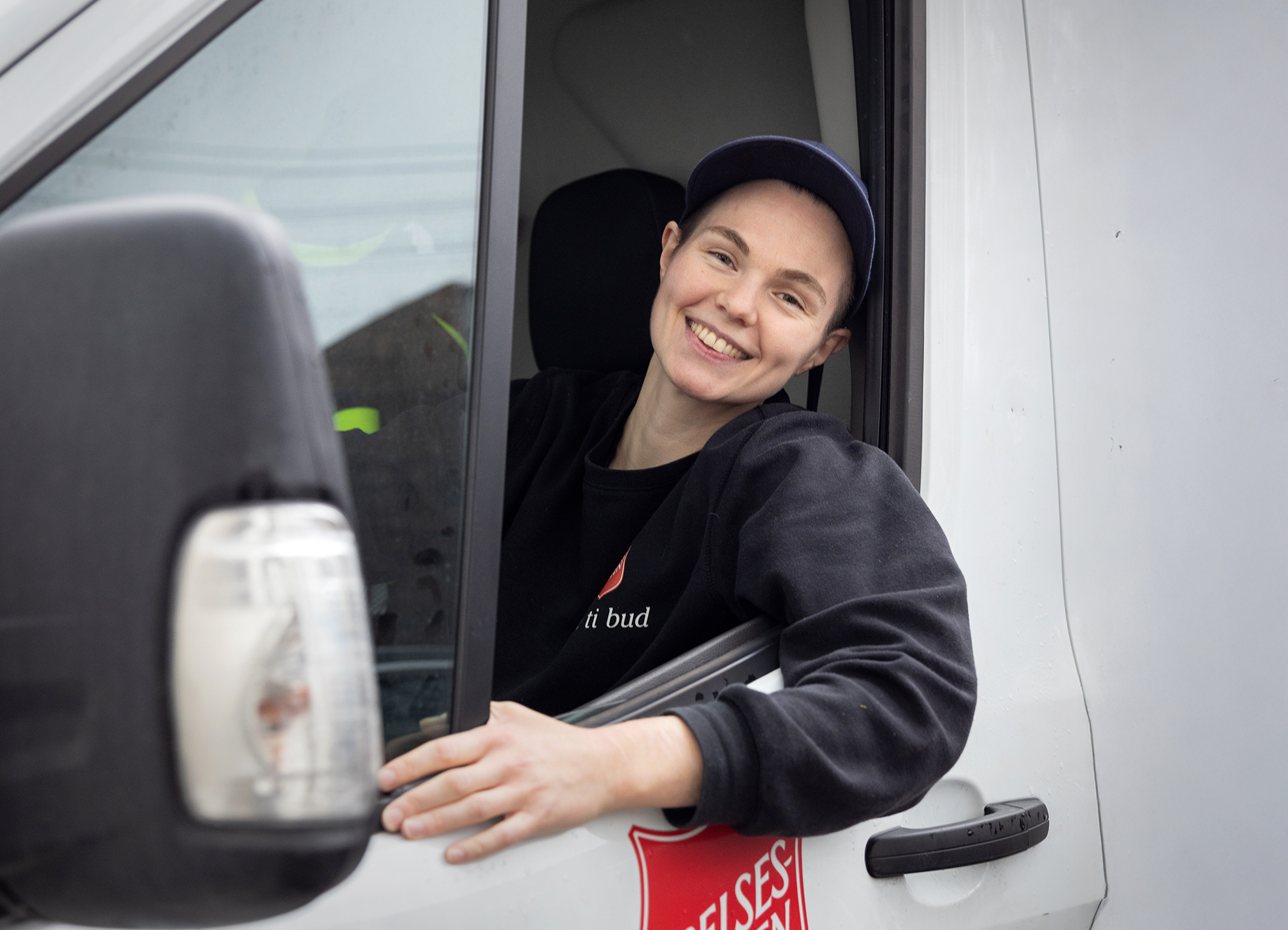 Foto: Kvinne tidlig i 30-årene med blå caps sitter i en hvit varebil fra Frelsesarmeen. Hun har vinduet nede og støtter hodet med venstre hånd.
