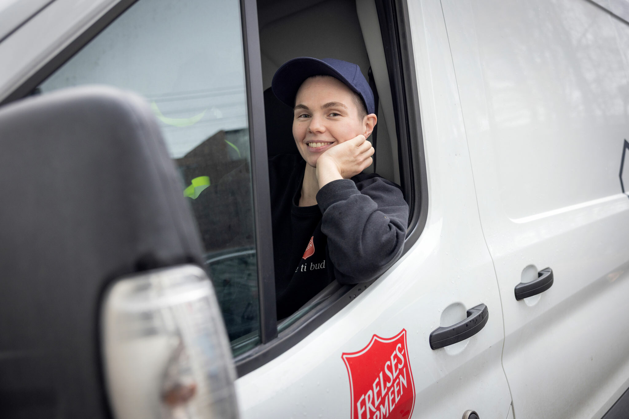 Foto: Kvinne tidlig i 30-årene med blå caps sitter i en hvit varebil fra Frelsearmeen. Hun har vinduet nede og støtter hodet med venstre hånd.