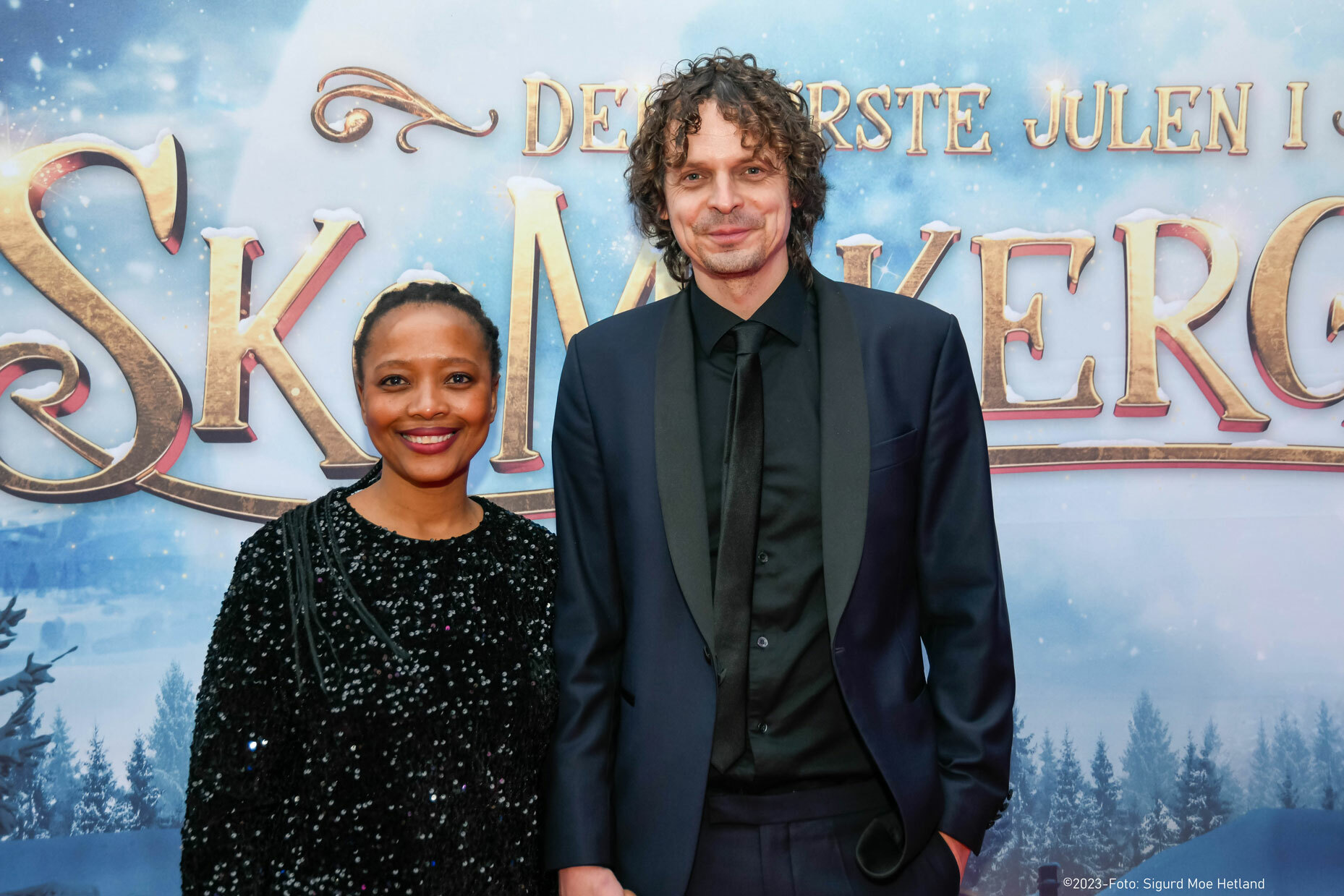 Svart kvinne med rastafletter og pen kjole. Hvit mann i svart dress og slips.