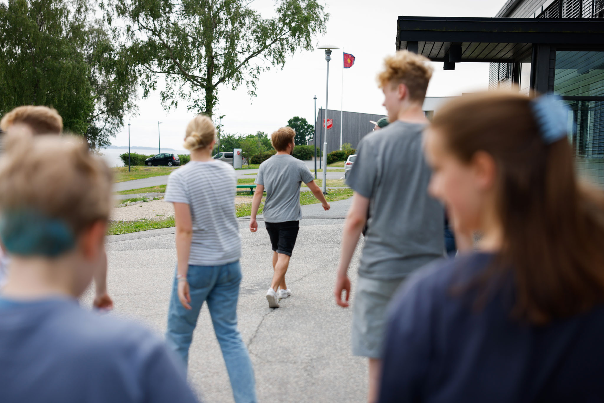 Foto: Barn og unge går mot et bygg det står skjoldet til Frelsesarmeen på. Et flagg med Blod og ild vaier i vinder. Det er sommer og grønne blader på trærne.