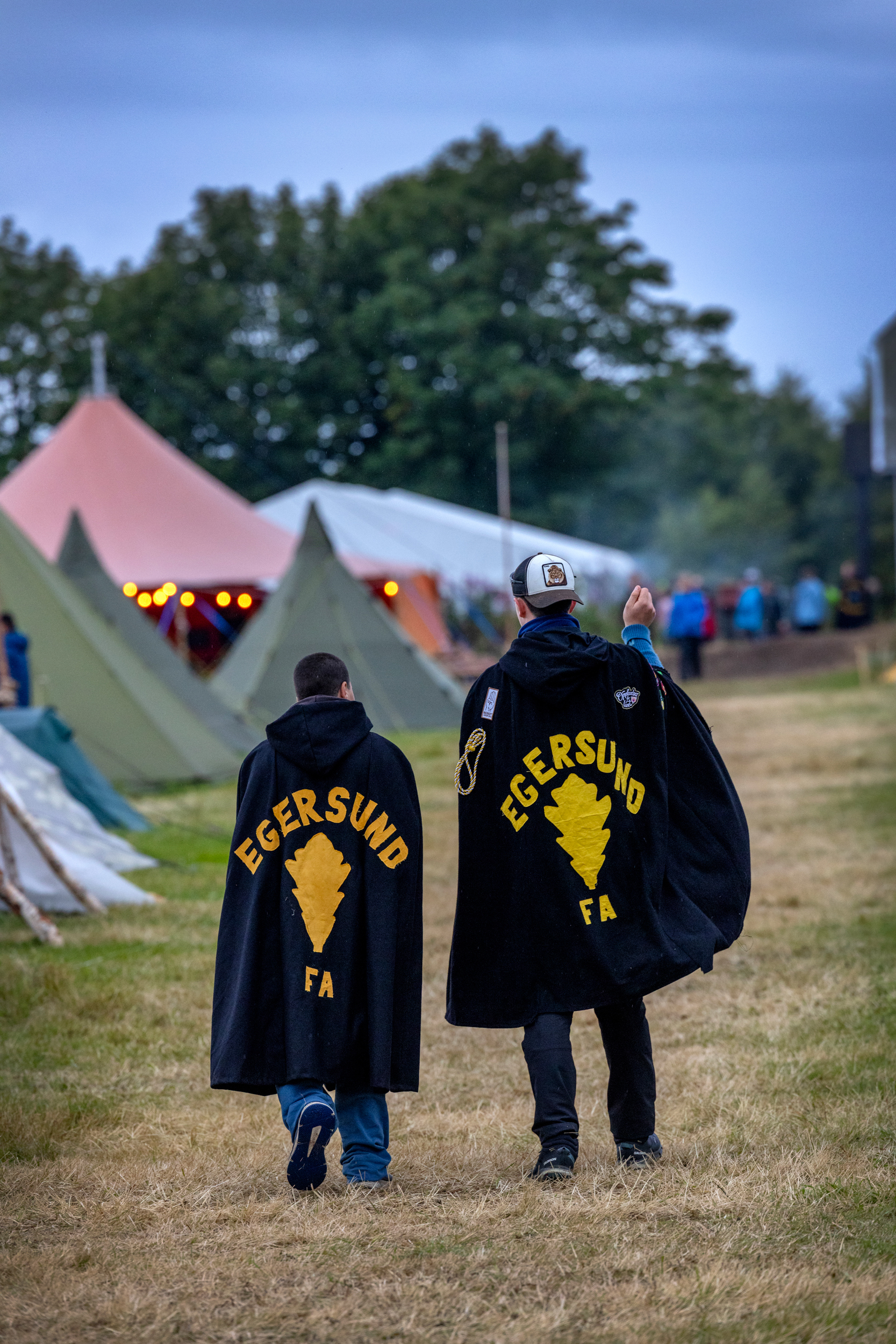 Foto: To speidere går bortover mot noen telt. Vi ser bare ryggen på dem der det står Egersund FA på ryggen.
