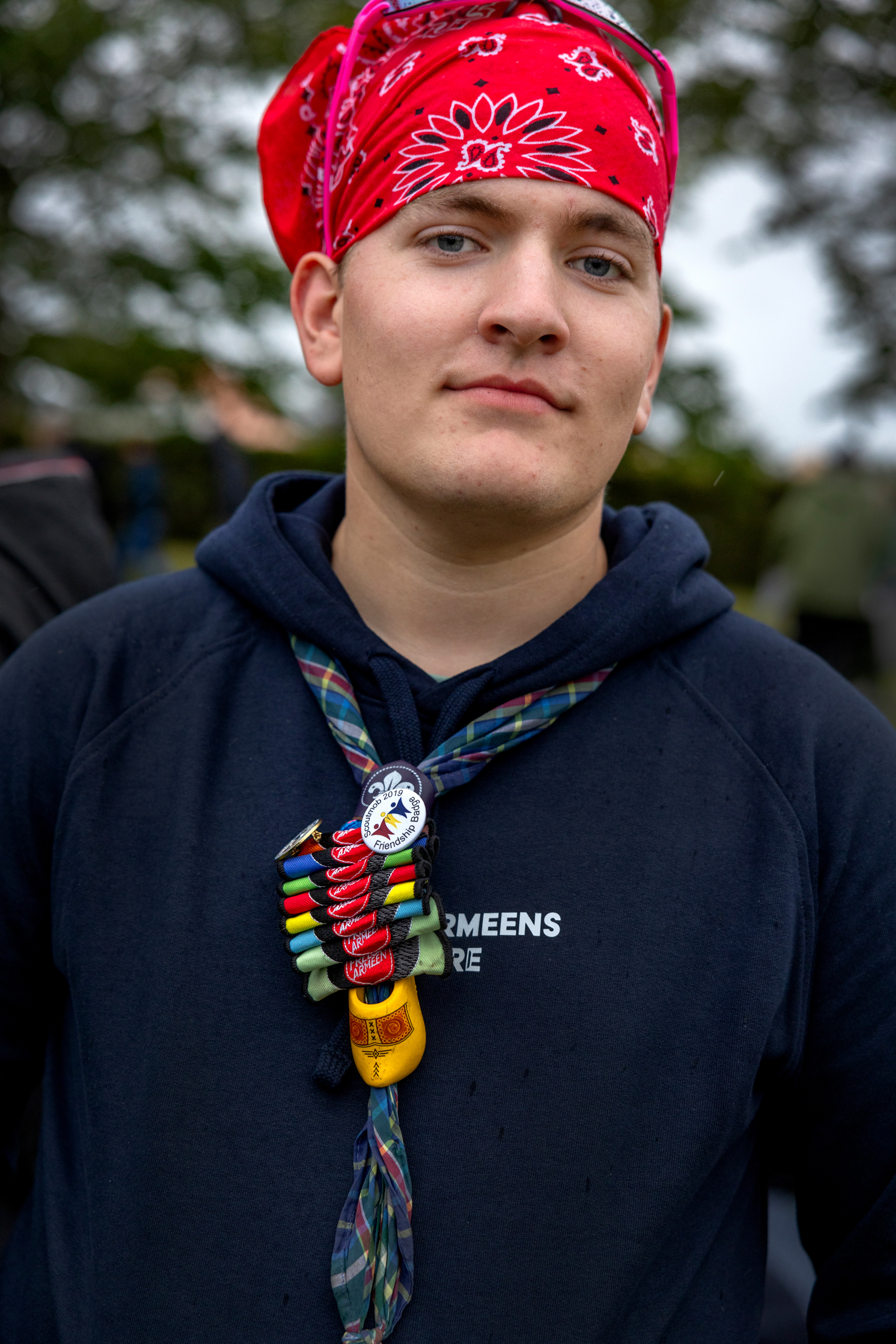 Foto: Ung mann med rød bandana på hodet og en blå hettegenser. Han har skjerf rundt halsen og en rekke speidermerker.