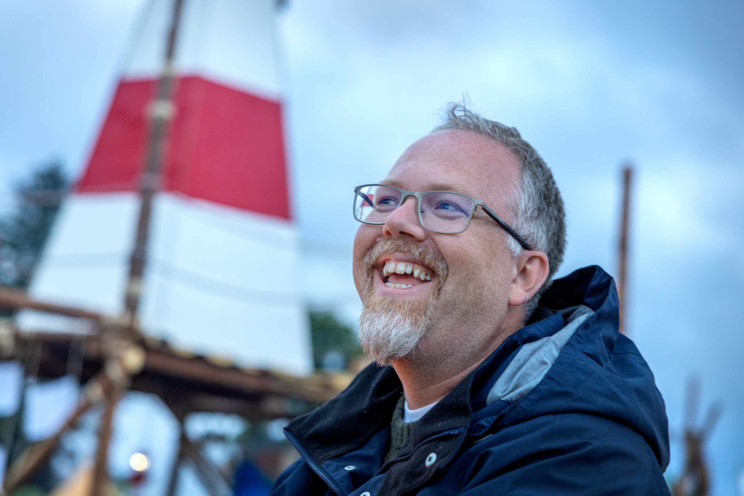 Foto: Mann som smiler godt mot noen andre. I bakgrunnen ses et fyrtårn i hvitt og rødt.