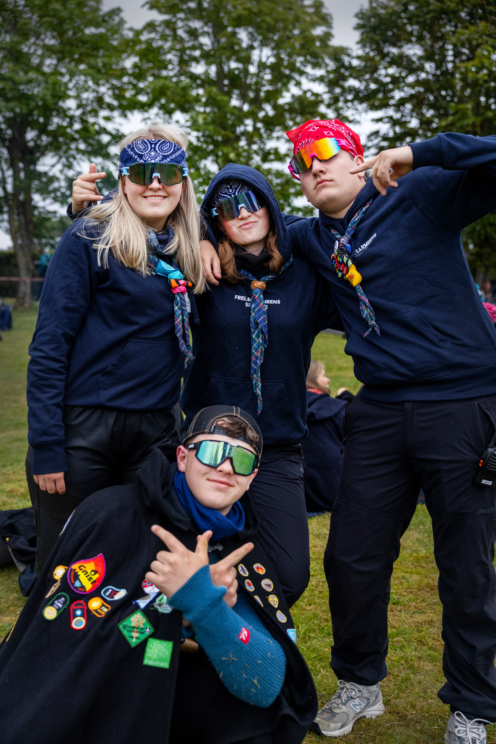 Foto: Bilde av fire ungdommer  – to jenter og to gutter – i speiderutstyr som tøffer seg litt med solbriller og bandana på et slags lagbilde.