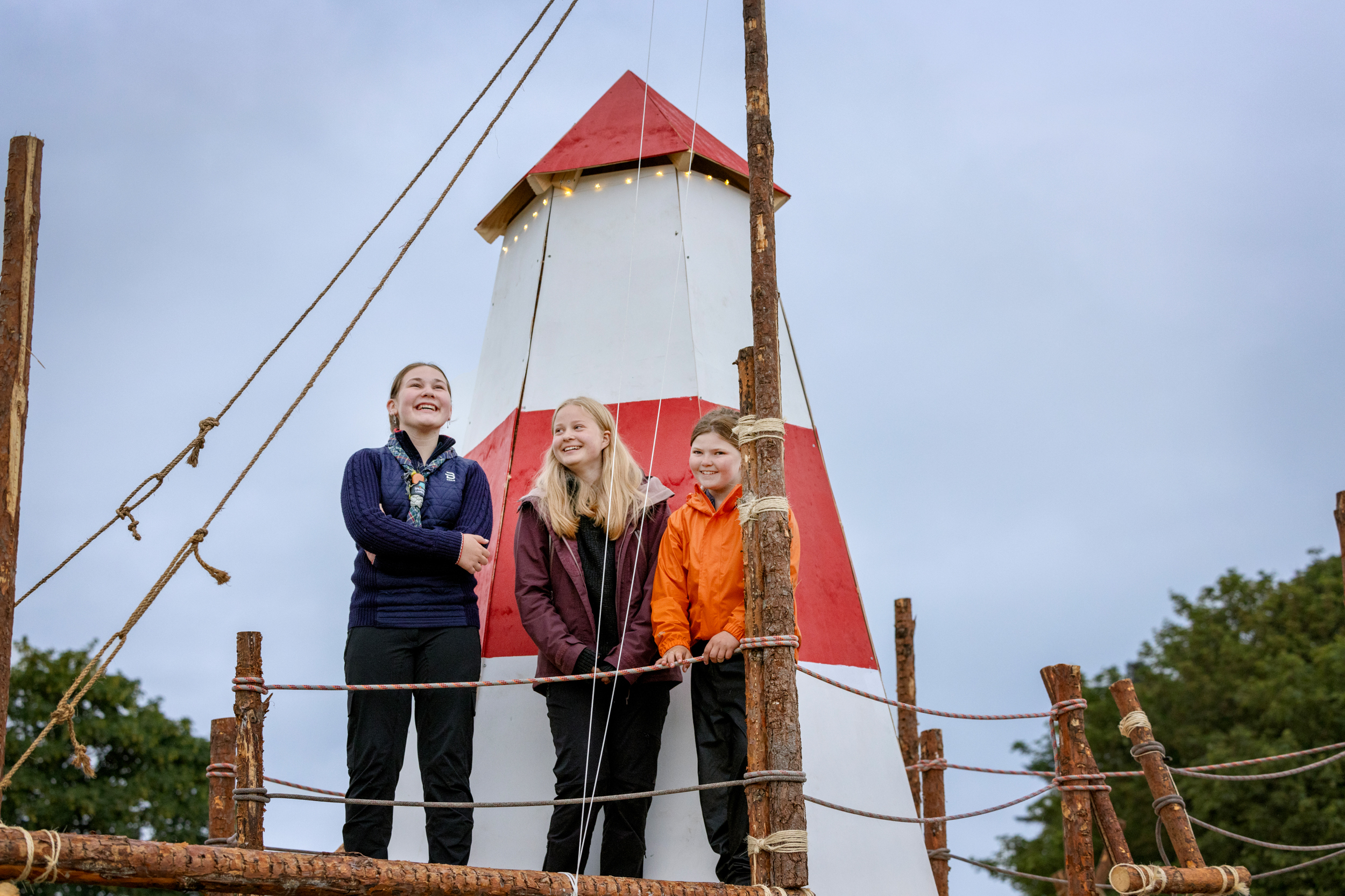 Foto: Tre jenter står på rekke oppe i et minifyrtårn i hvitt og rødt tre.