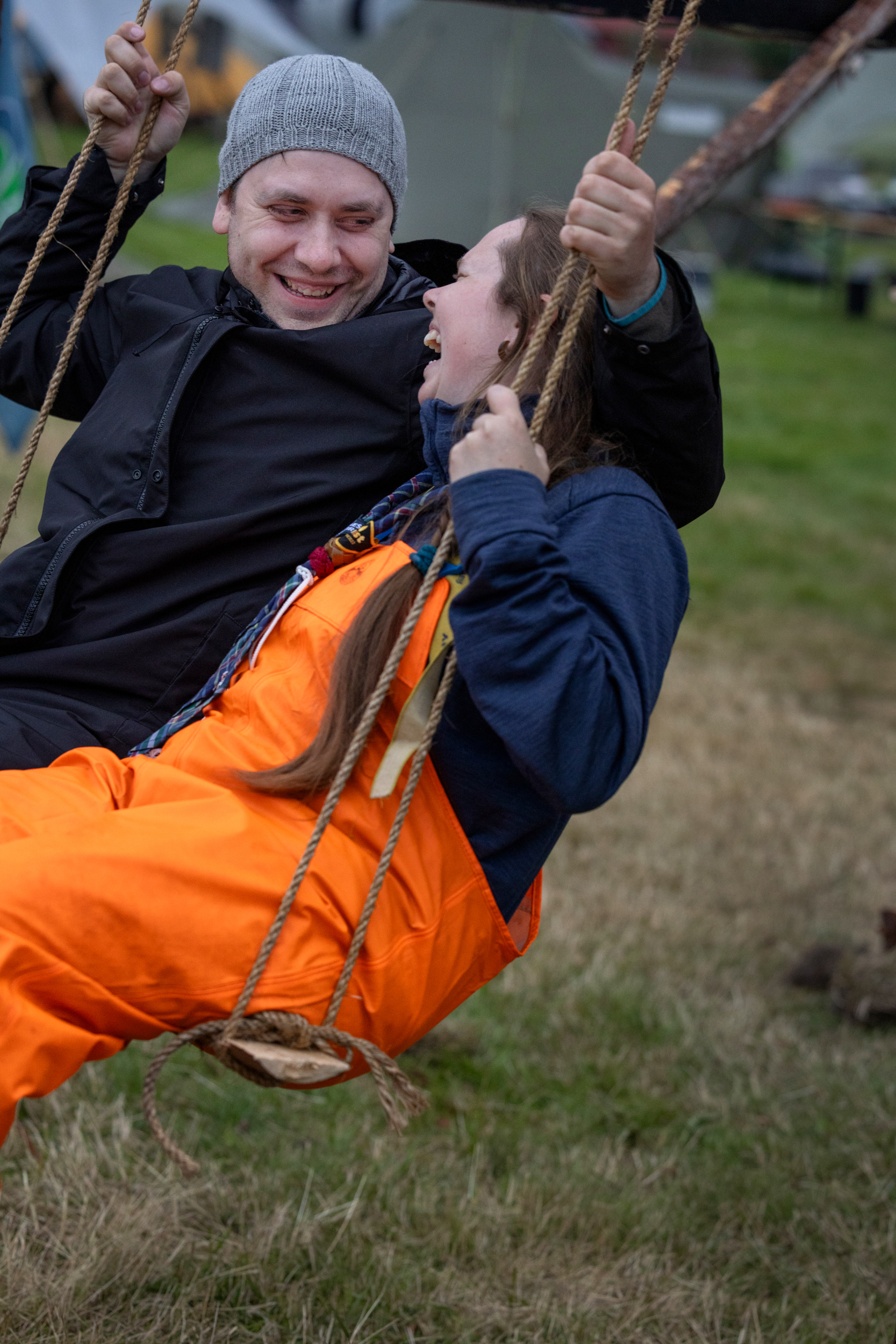 Foto: To voksne mennesker i regntøy sitter på samme huske.