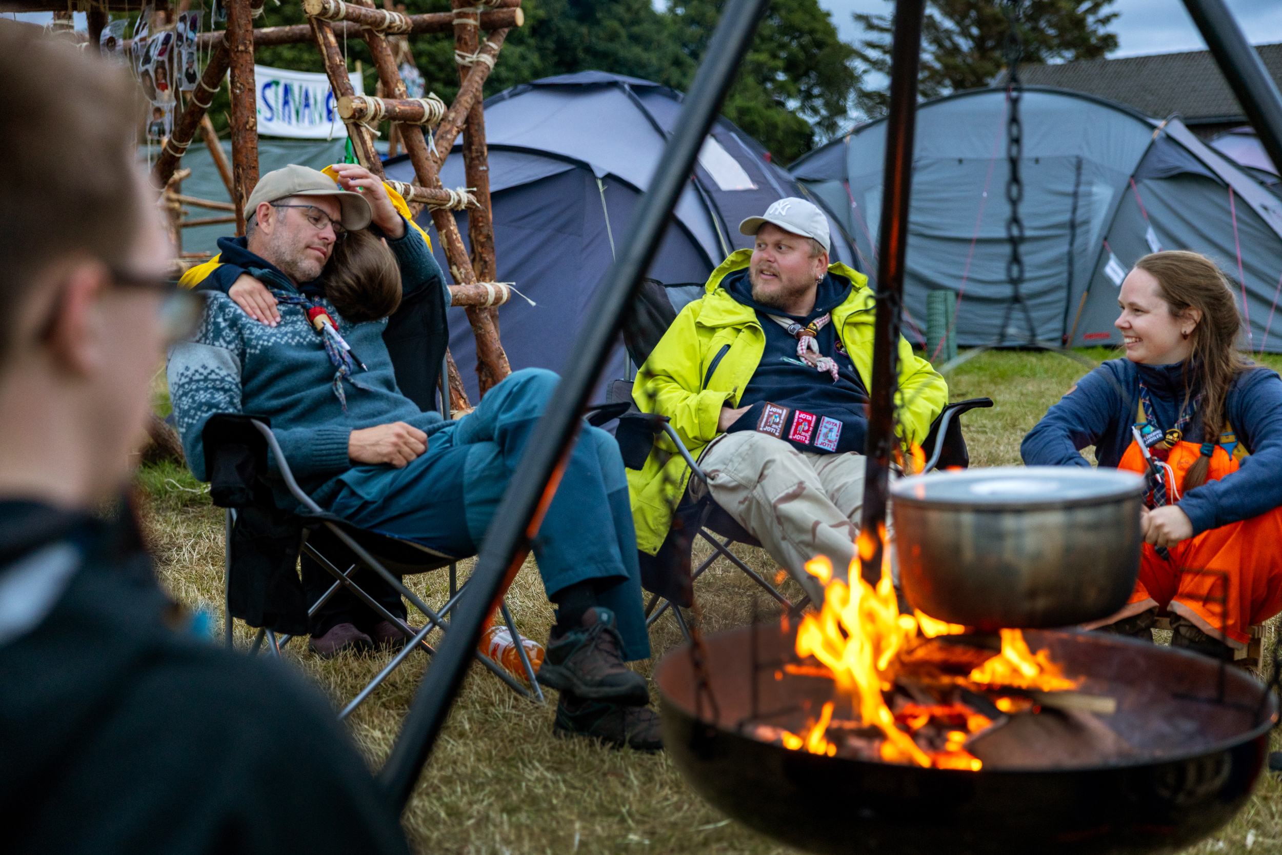 Foto: Tre voksne personer i varmt tøy rundt en bålpanne med fyr i. Et barn klemmer den ene voksne bakfra og en ungdom sitter med ryggen til, på den andre siden.