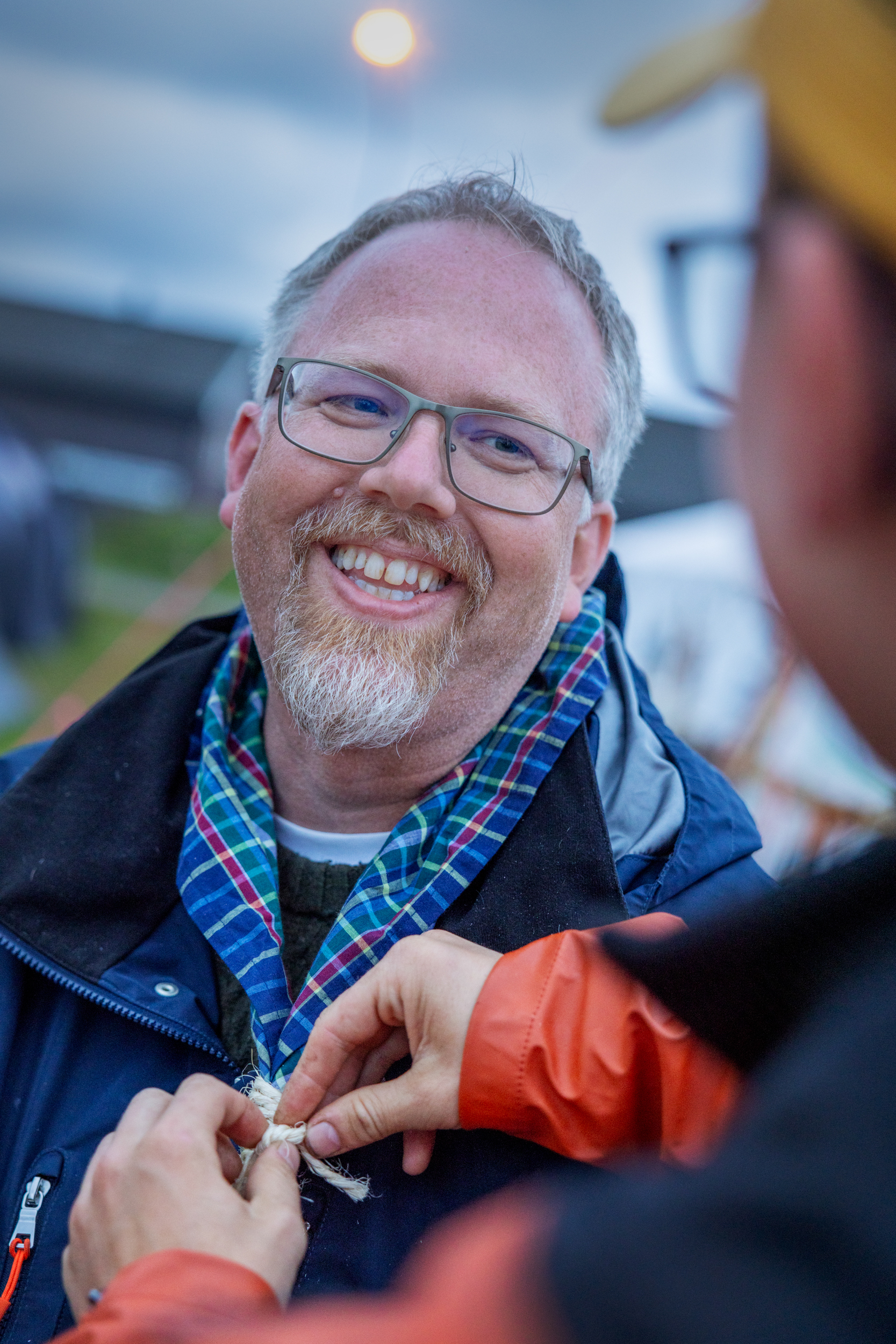 Foto: Av en mann midt i livet som får knyttet speiderknuten av en yngre fyr.