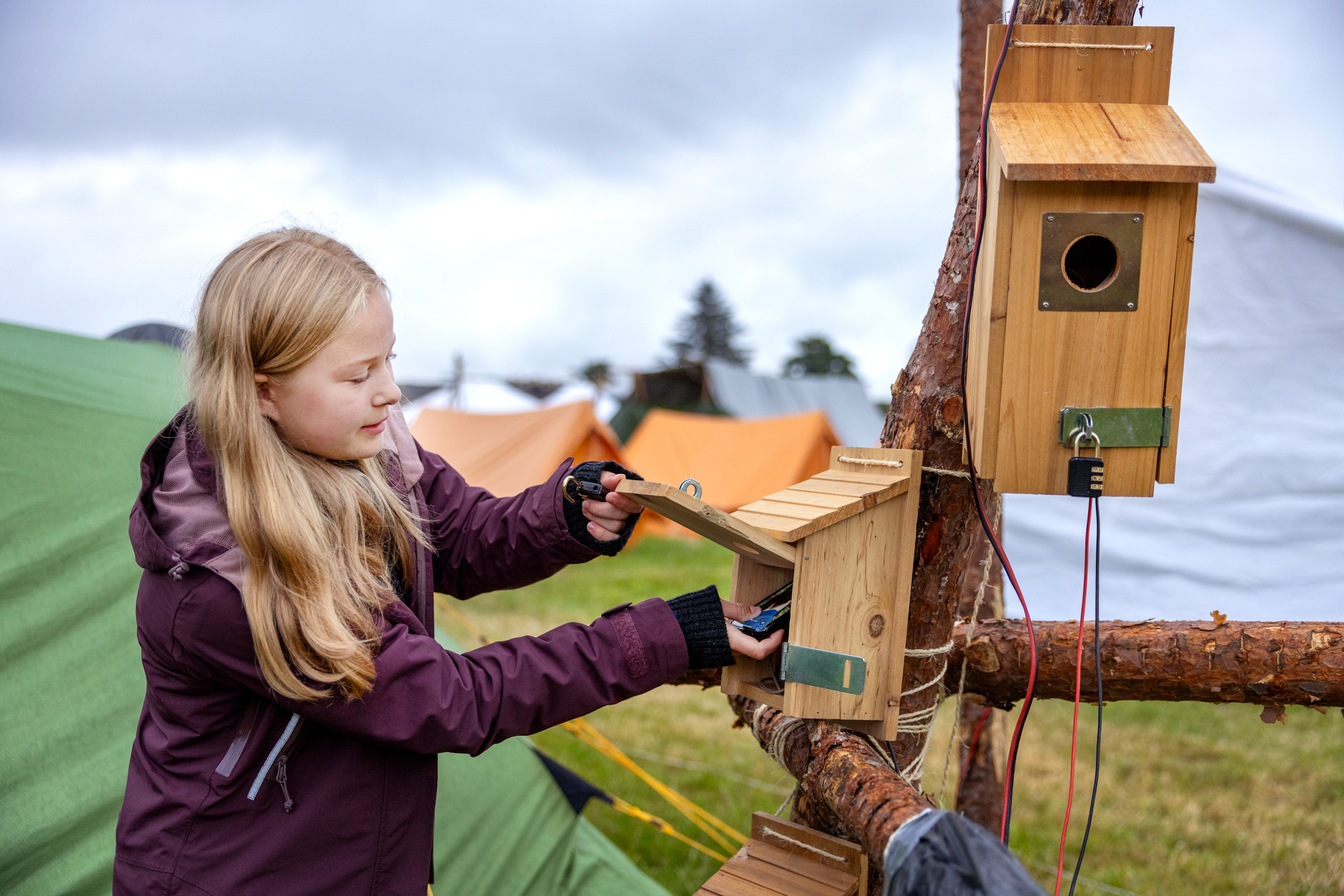 Foto: Tenåringsjente legger mobilen inn i det som ser ut som en fuglekasse med hengelås på.