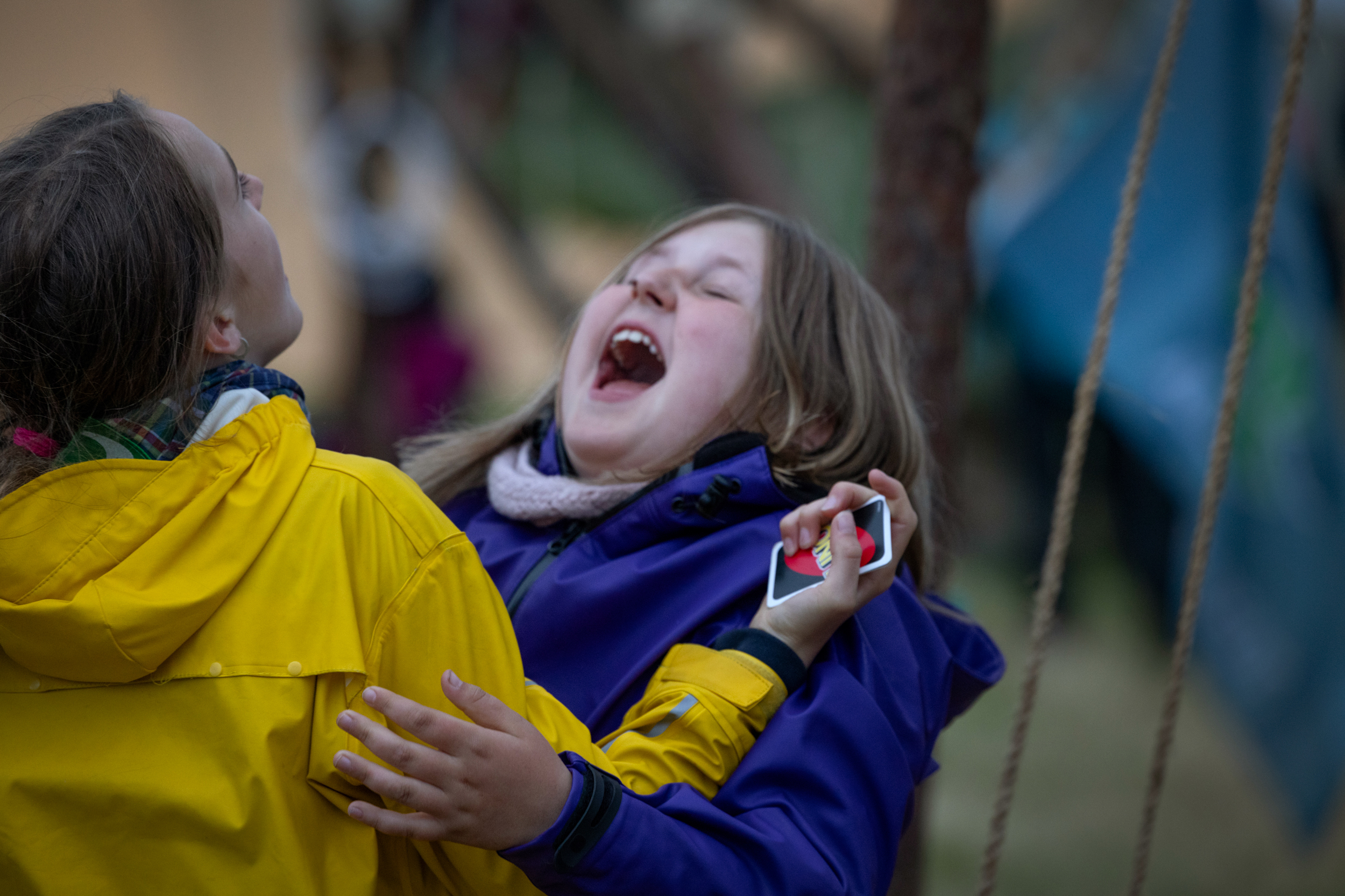 Foto: To jenter i regntøy gapskratter. Hun ene har en kortstokk i hånden.