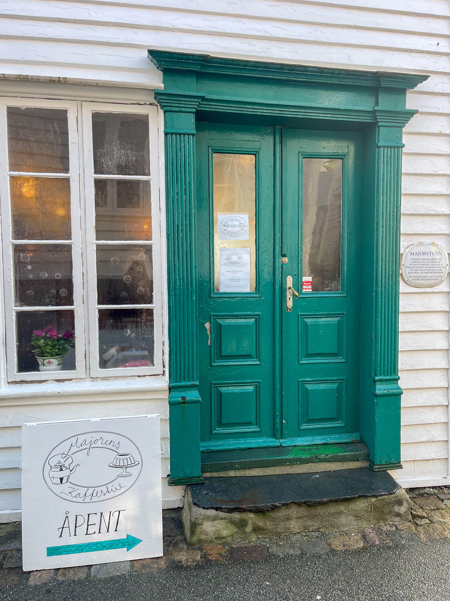 En gammel, dobbel dør med et gammelt vindu med åtte små ruter. Utenfor står et skilt til en kafé.