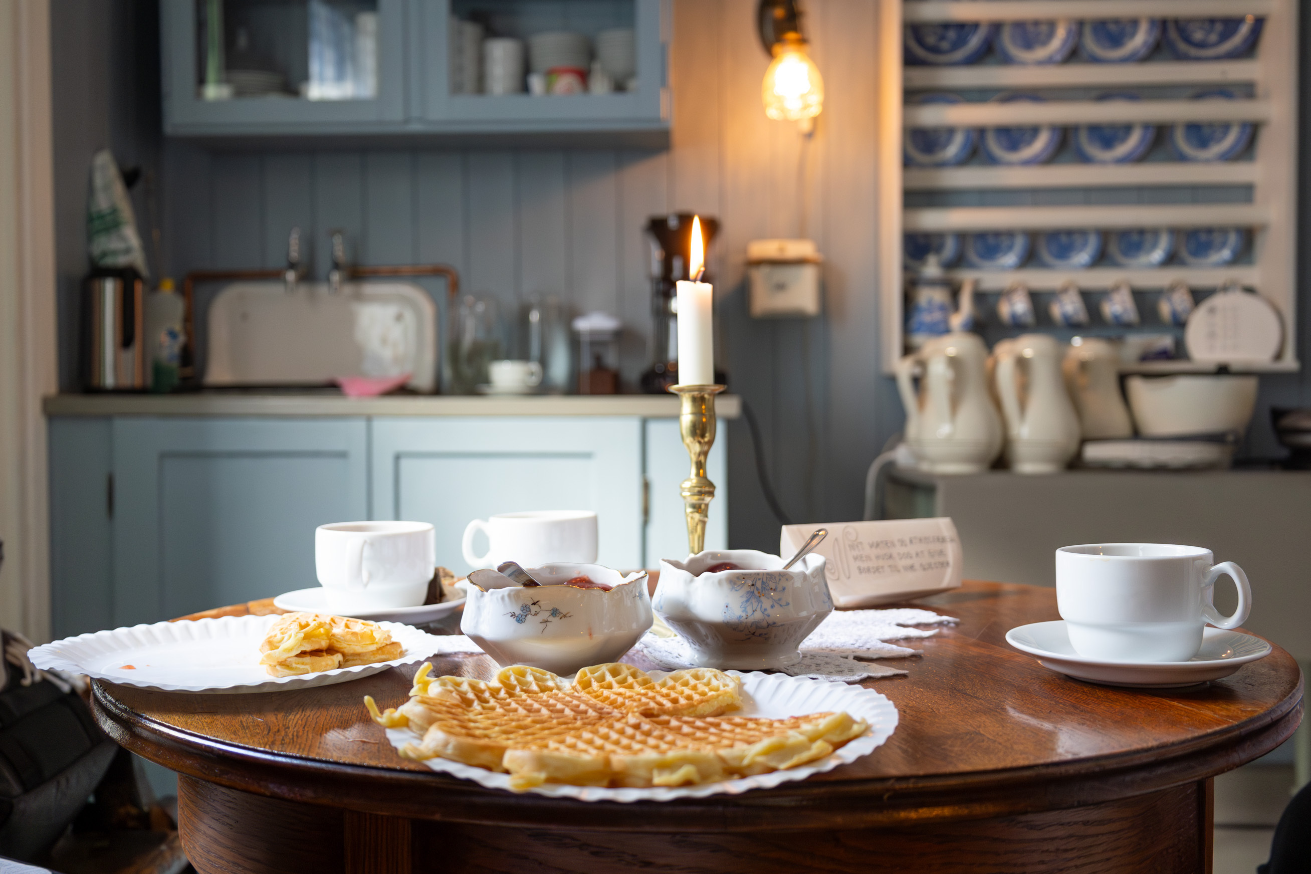Dekket bord med lys og gammelt servise. Her ligger halvspiste vafler. I bakgrunnen er resten av kjøkkenet i gammel stil.