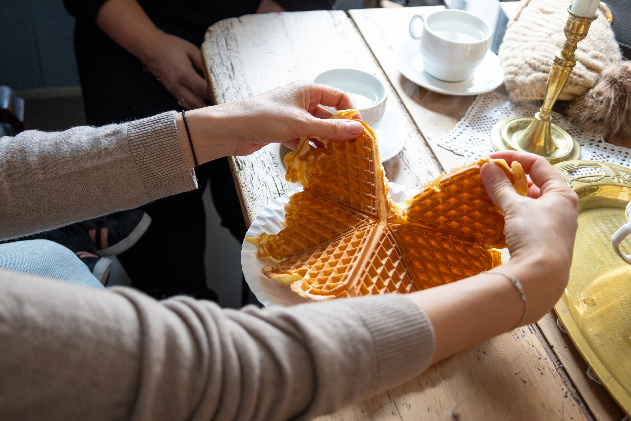 To bilder ved siden av hverandre der vi først ser to unge kvinner som ligner på hverandre i en sofa, deretter er det nærbilde av en av dem som river opp et vaffelhjerte på tallerken.