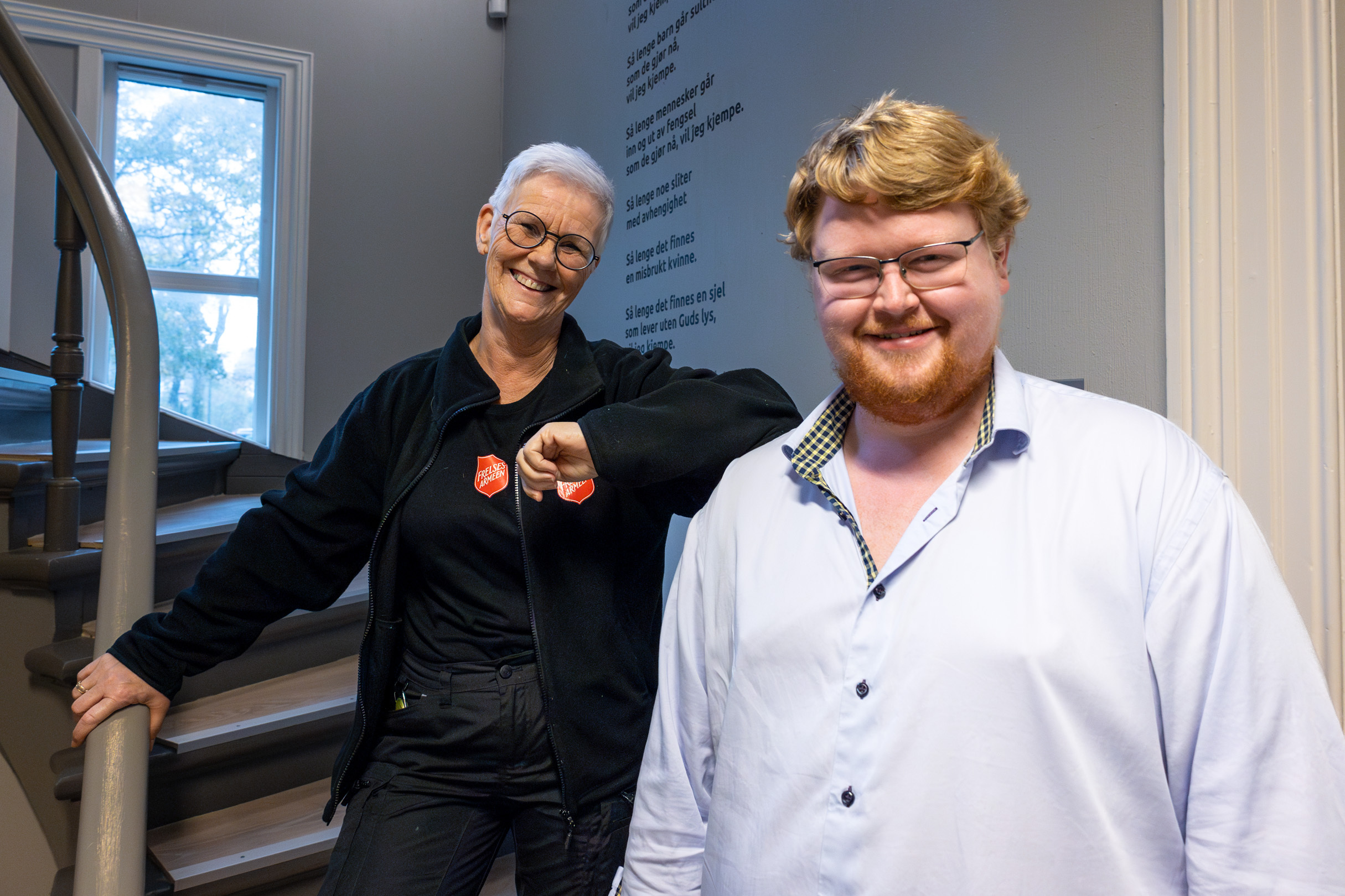 Voksen kvinne og ung mann står i trappa inne i et gammelt hus.