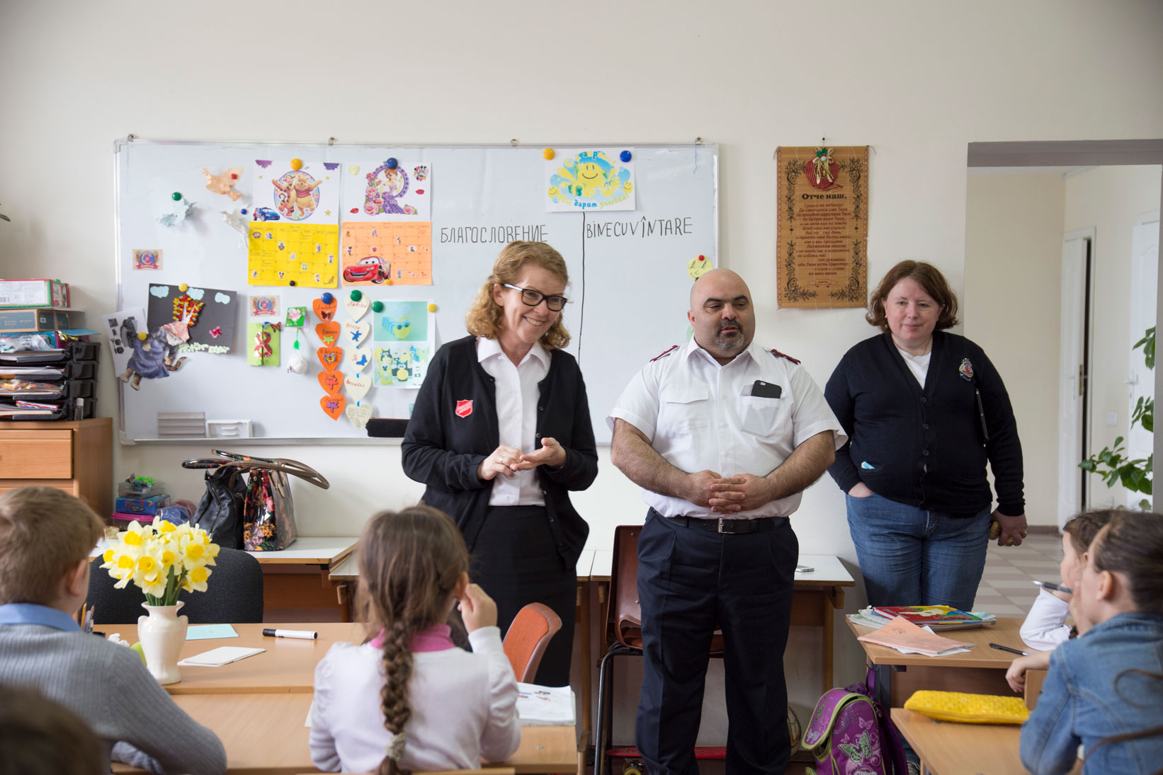 En dame i frelsesarmeuniform står sammen med barn i et klasserom.