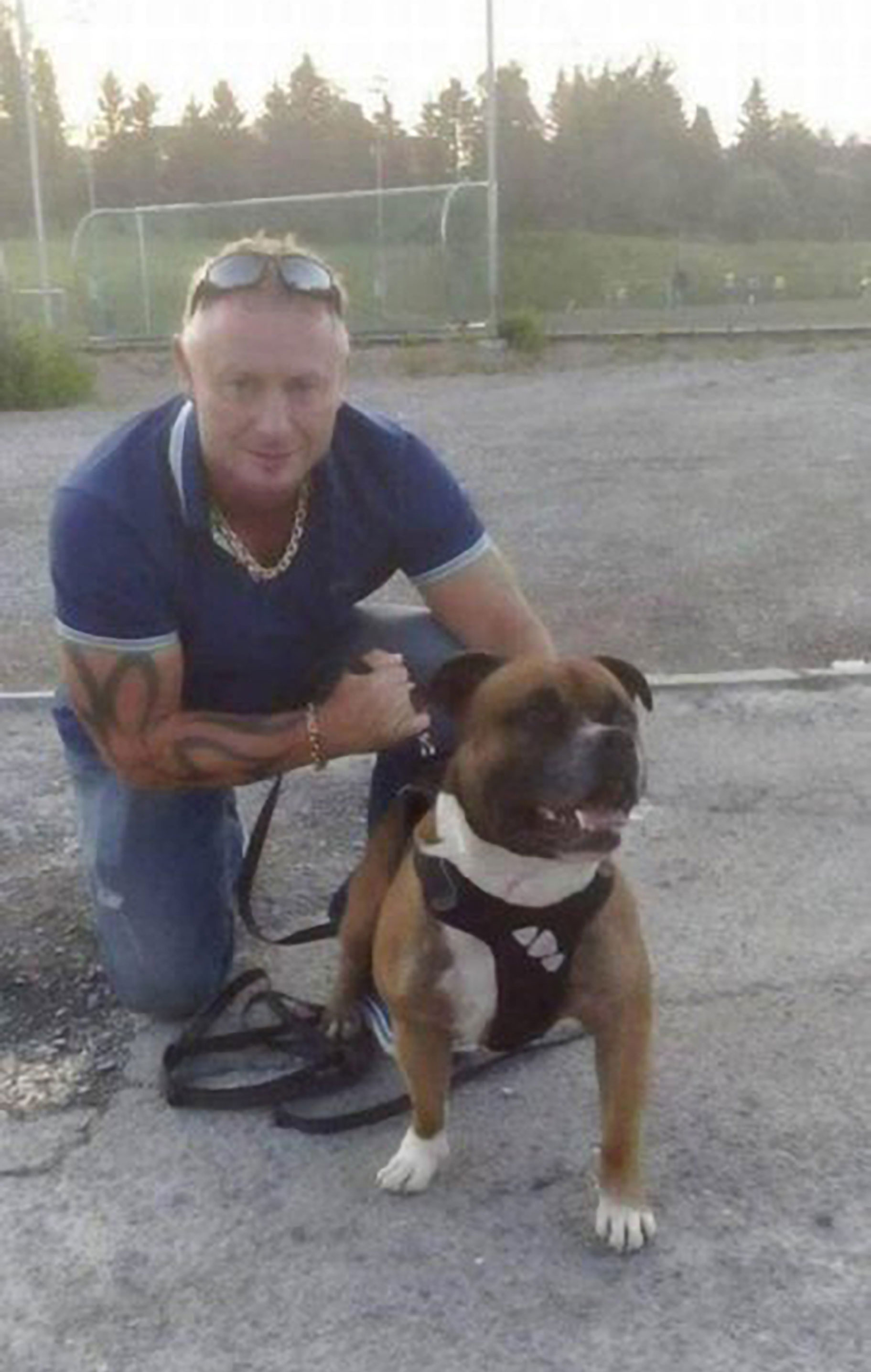 Foto: Mann i blå T-skjorte sitter på huk sammen med en hund. Han har tatoveringer.