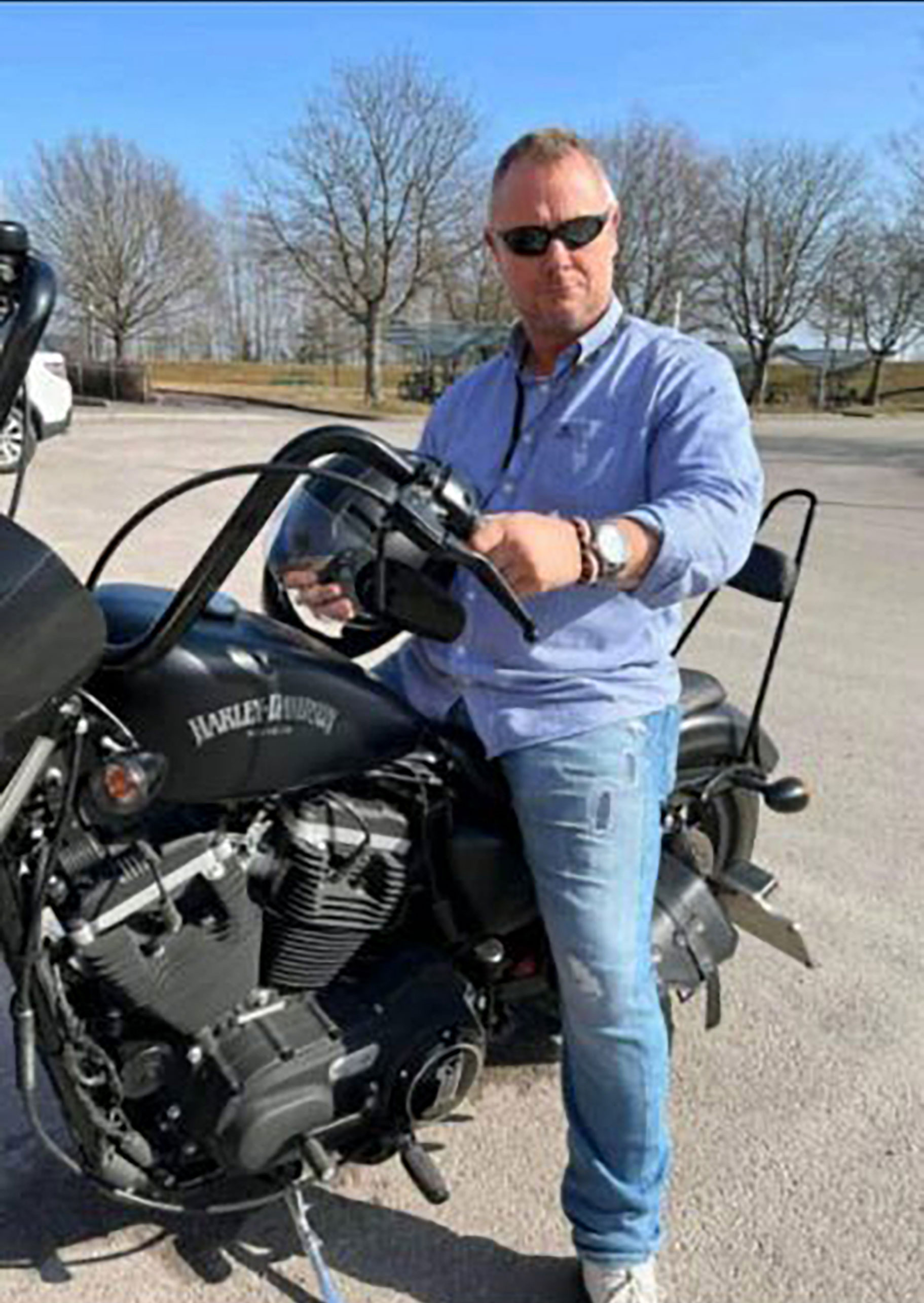 Foto: Mann med lyseblå skjorte og solbriller sitter på en parkert motorsykkel.