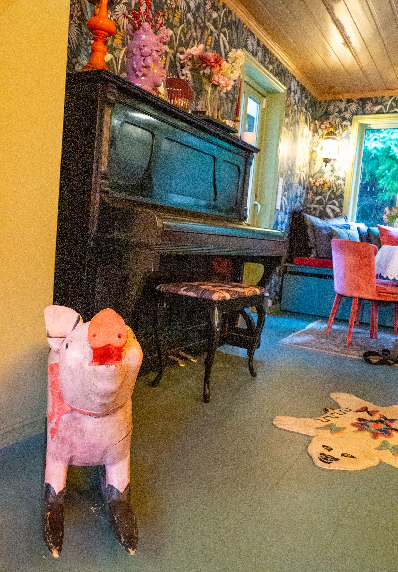 Foto: Interiør med rosa gris på meier og ellers blomstrete tapet og et piano langs veggen.