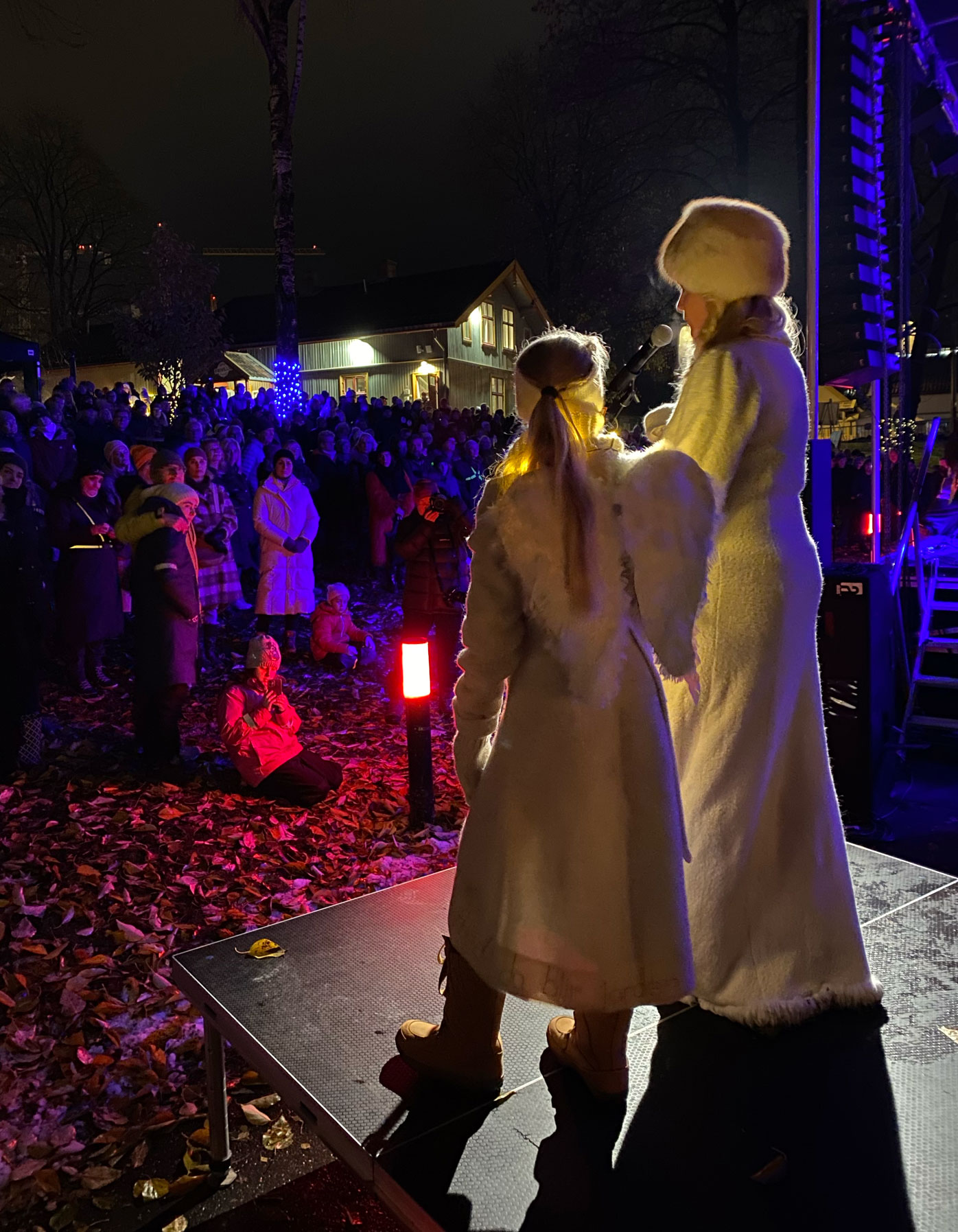 Foto: To personer står på en scene utendørs i mørket. Det blått og rødt lys og mange folk har møtt opp.