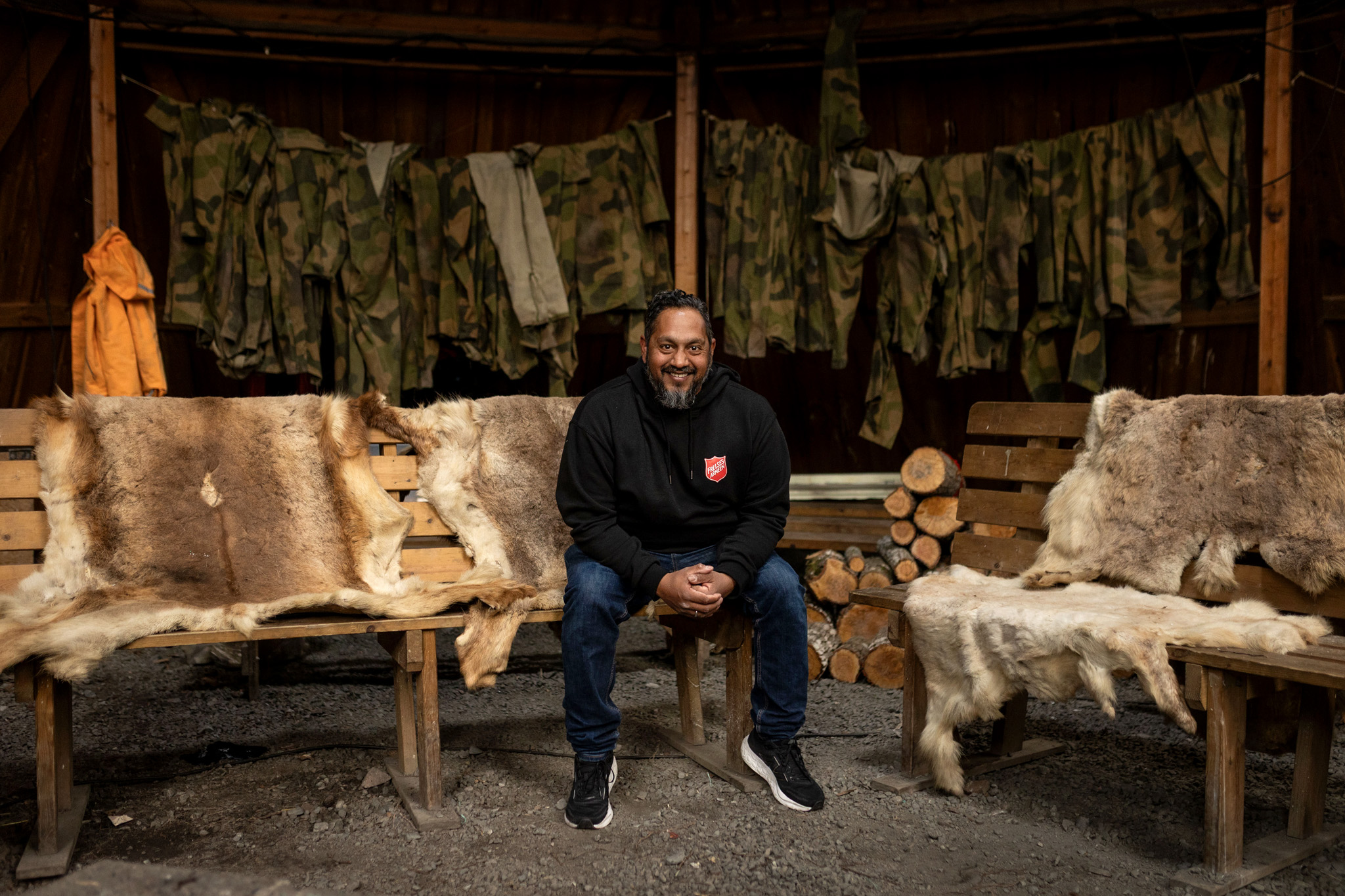 Foto: Mann som sitter på en enkel benk dekket av reinsdyrskinn.