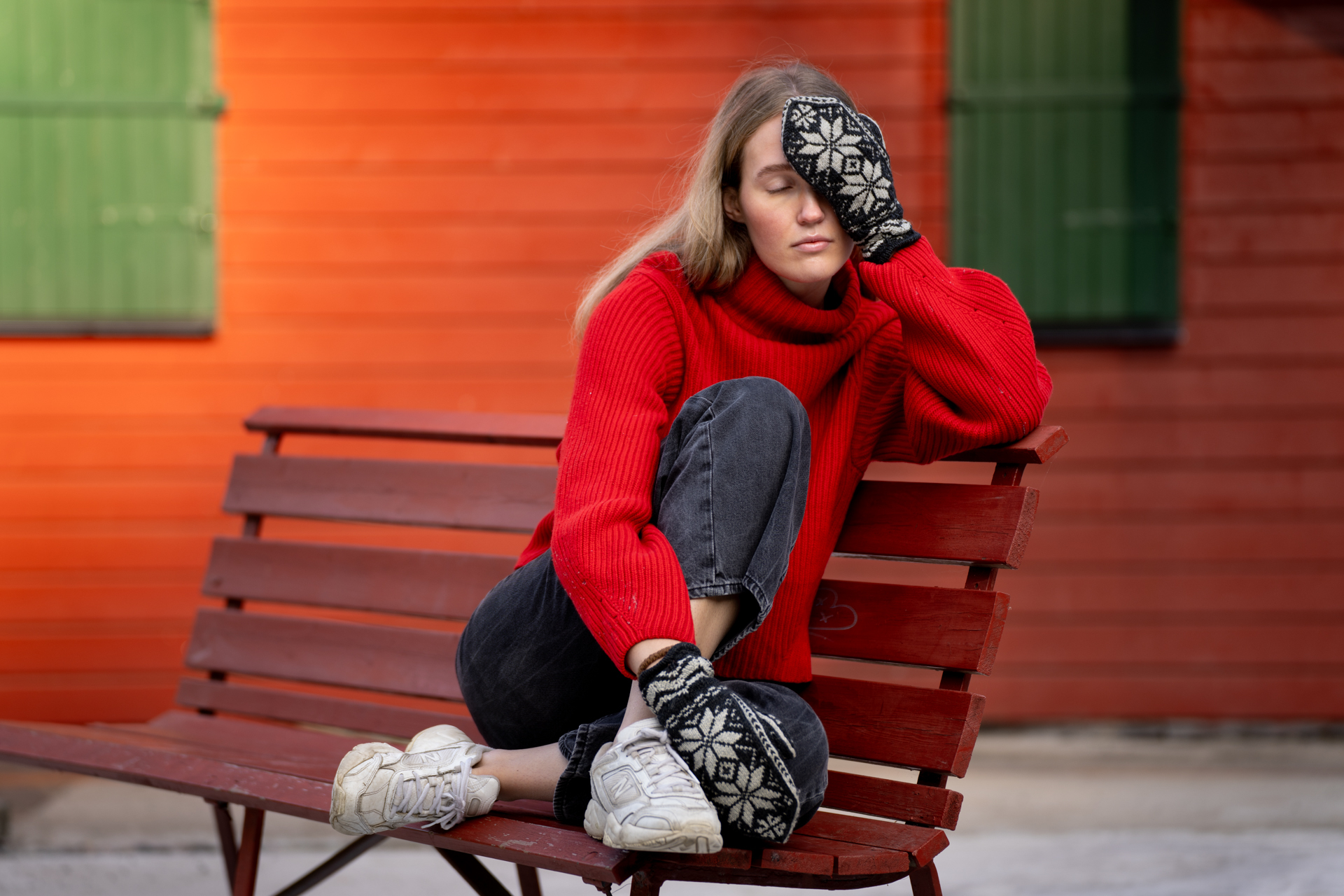 Ansiktet til en ung kvinne med langt, mellomblondt hår og rød genser. Hun holder en selbuvott foran venstre øye og dekker dermed halve ansiktet.