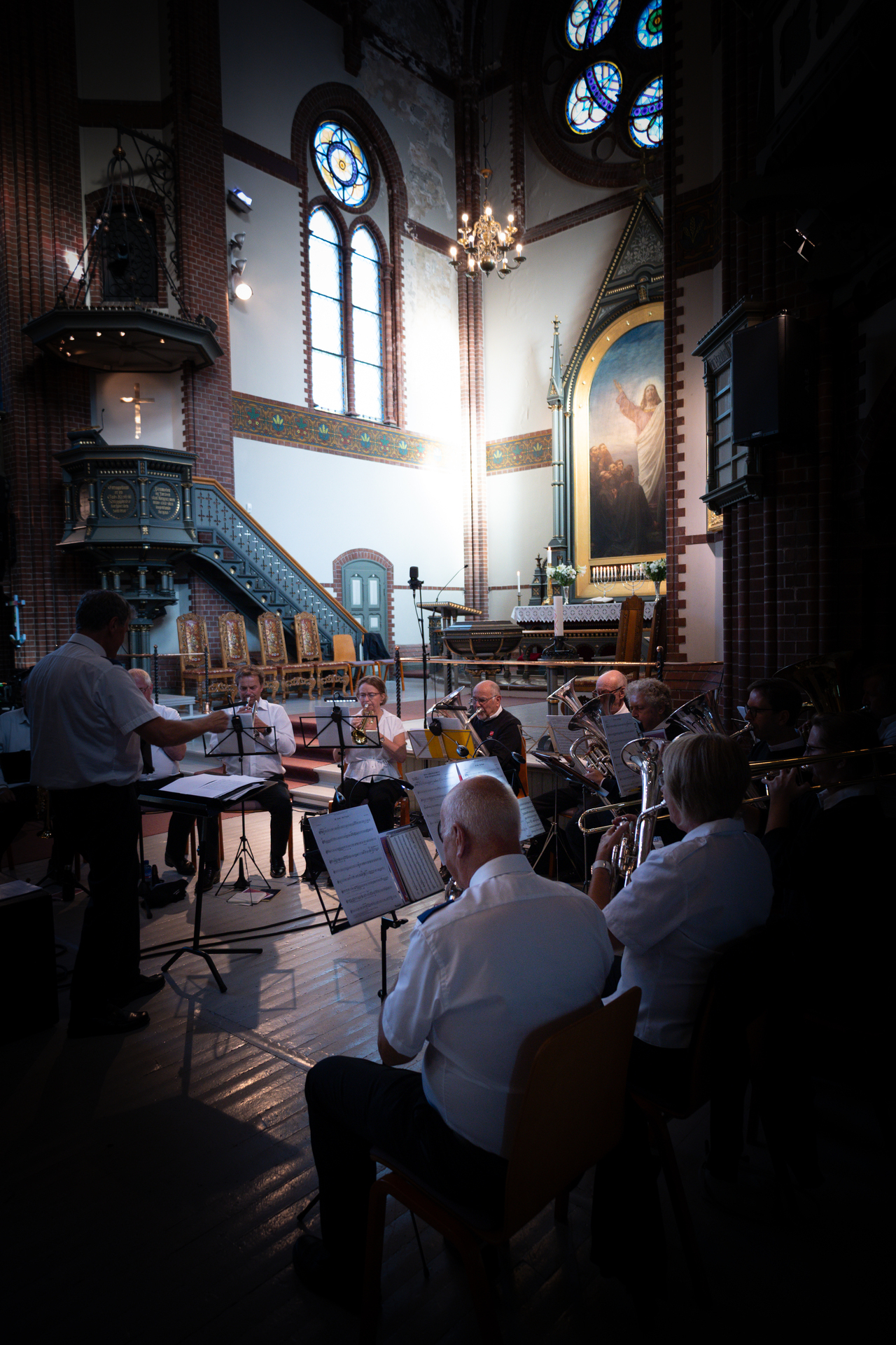 Foto: Kirkerom med folk som sitter i salen. Flere av vinduene har glassmalerier.