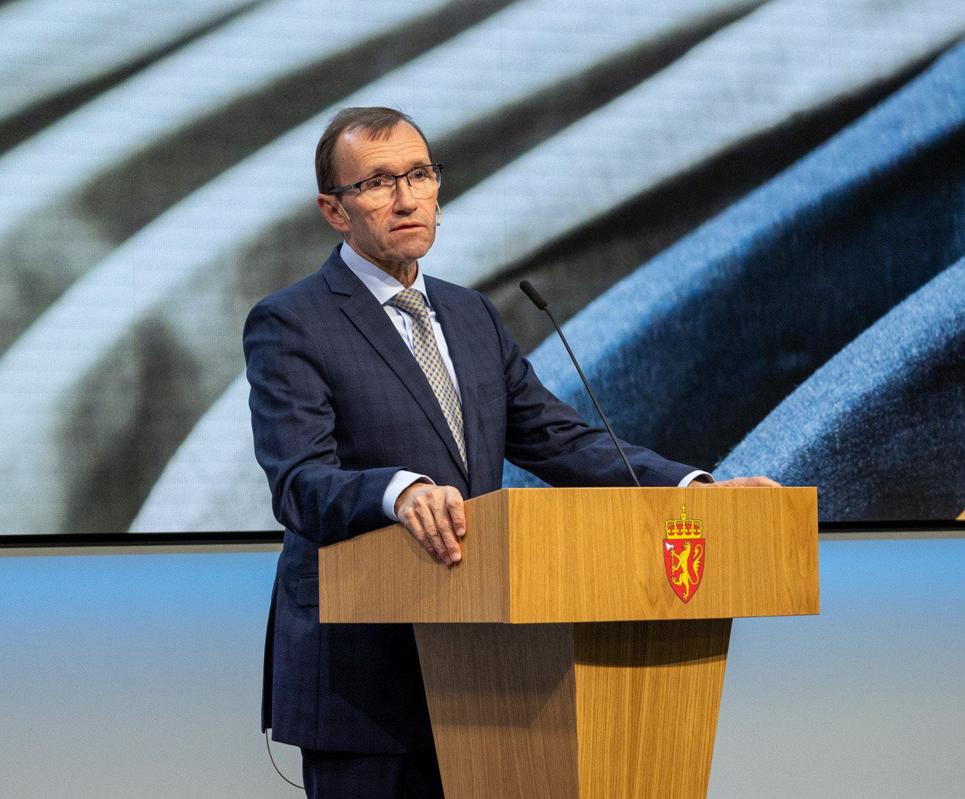 Mann med briller står på en talerstol med det norske riksvåpenet. Dette er Espen Barth Eide da han var klima- og miljøminister.