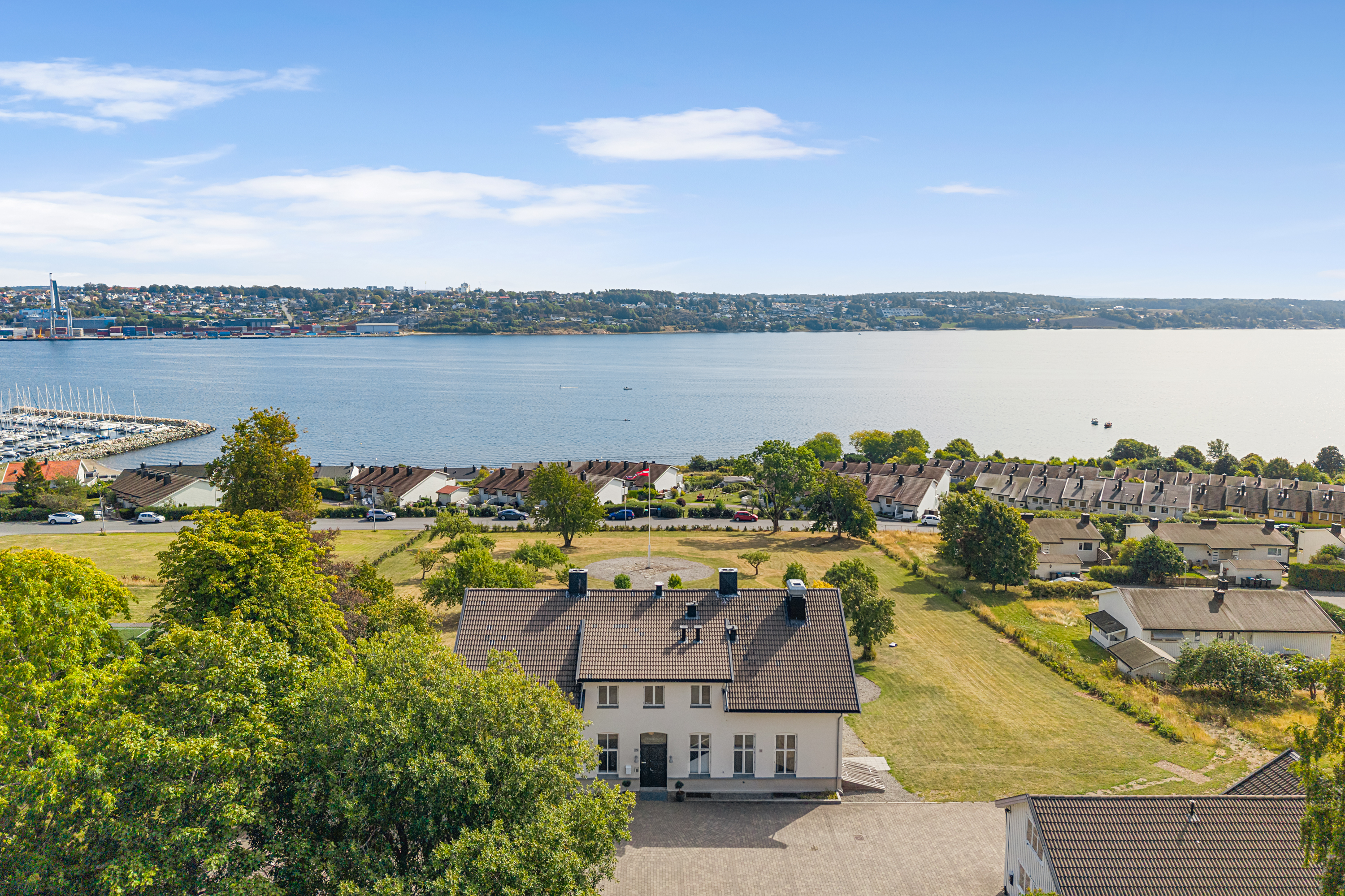 Bilde 1: Utsiktsbilde over hagen med vimpel på flaggstang i hagen, sjø i bakgrunnen og Bastø Fosen (ferje). Bilde2: Dronebilde av gammelt herskapelig stort hus, nabohus rundt og sjøen nedenfor.