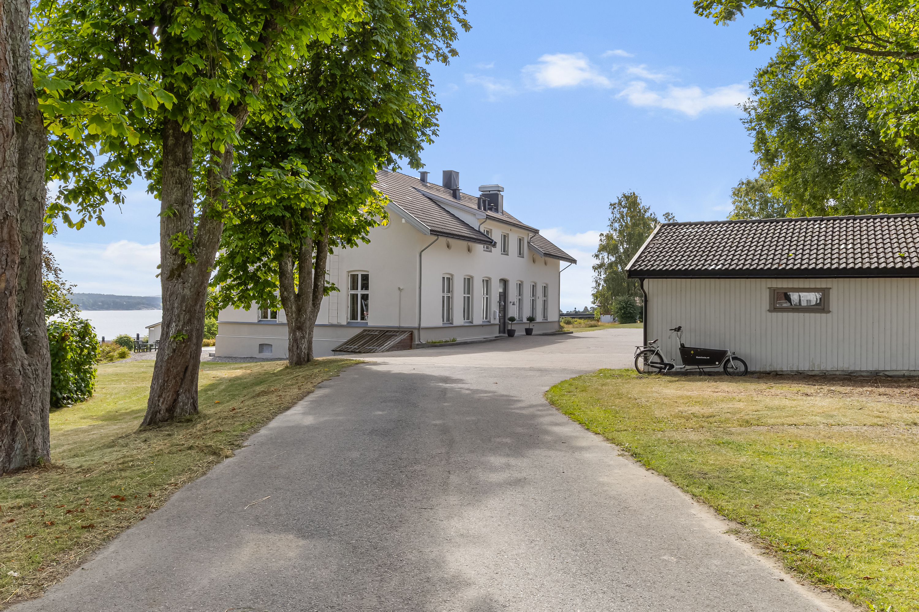 Allé ned mot gammelt, hvit, herskapelig hus. Hvit garasje til høyre. Store kastanje trær til venstre i bilde.