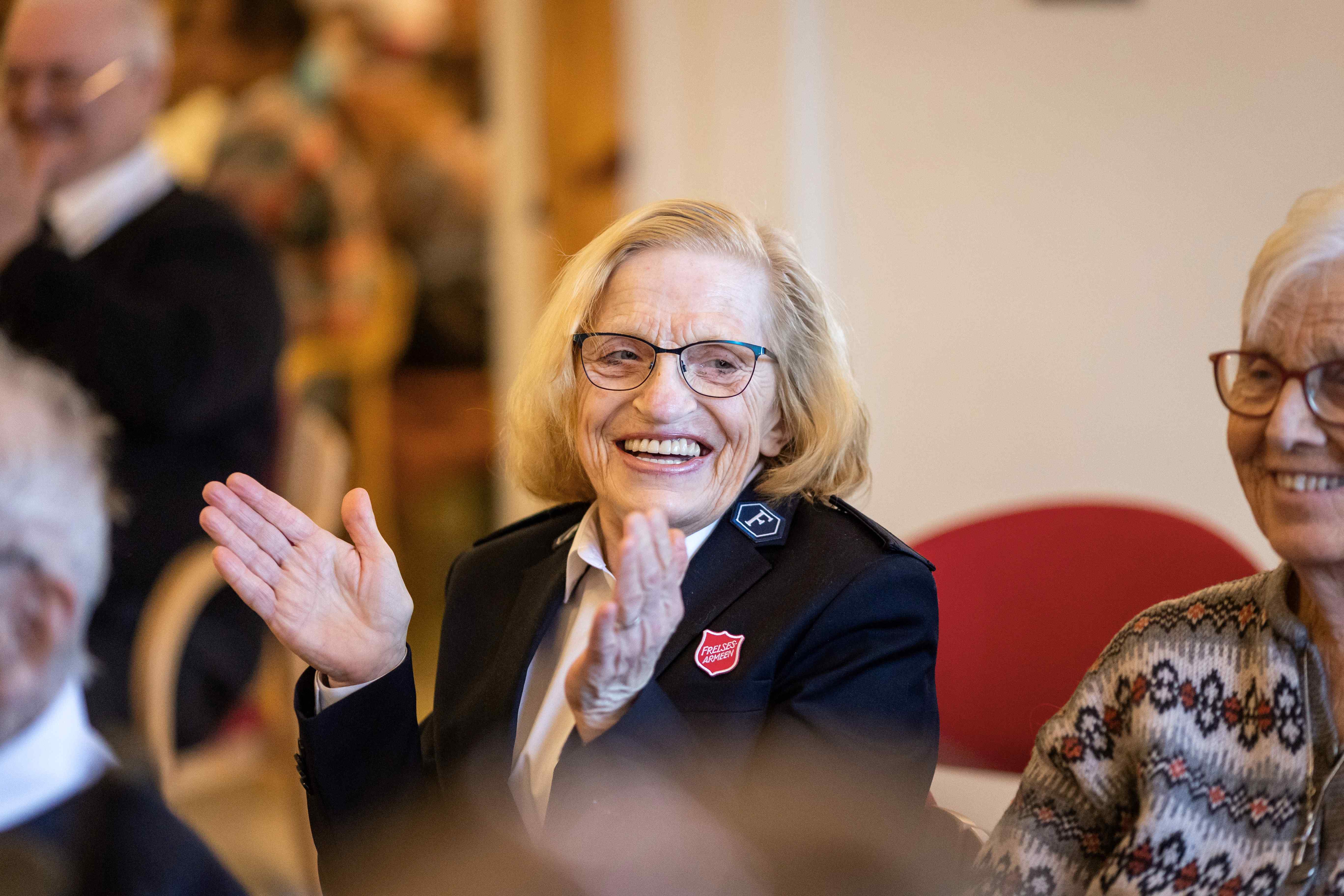 Eldre dame i Frelsesarmeens uniform smiler og klapper i hendene