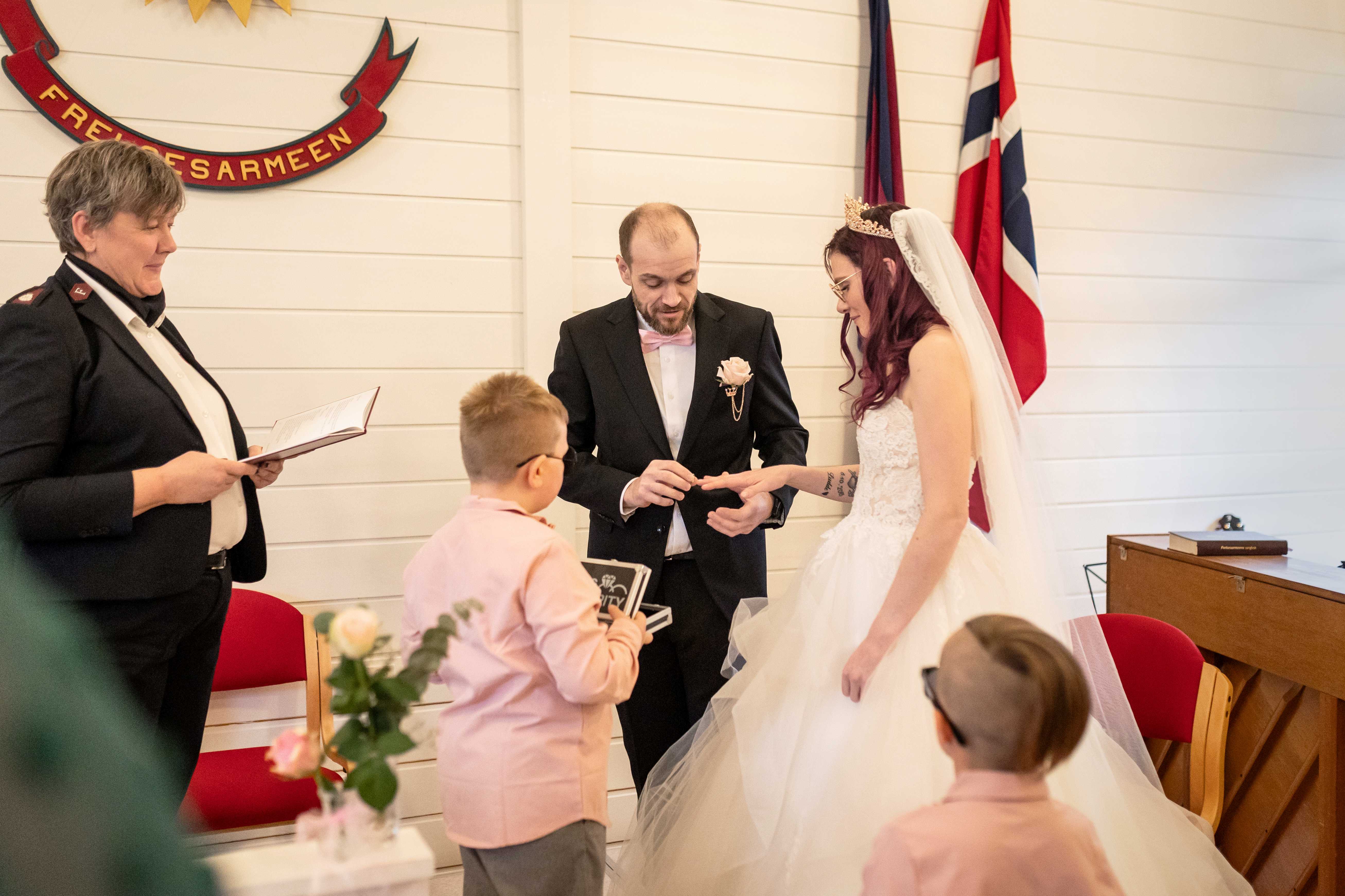 Bruden får ring på fingweren av brudgommen mens Line og to unge brudesvenner ser på.