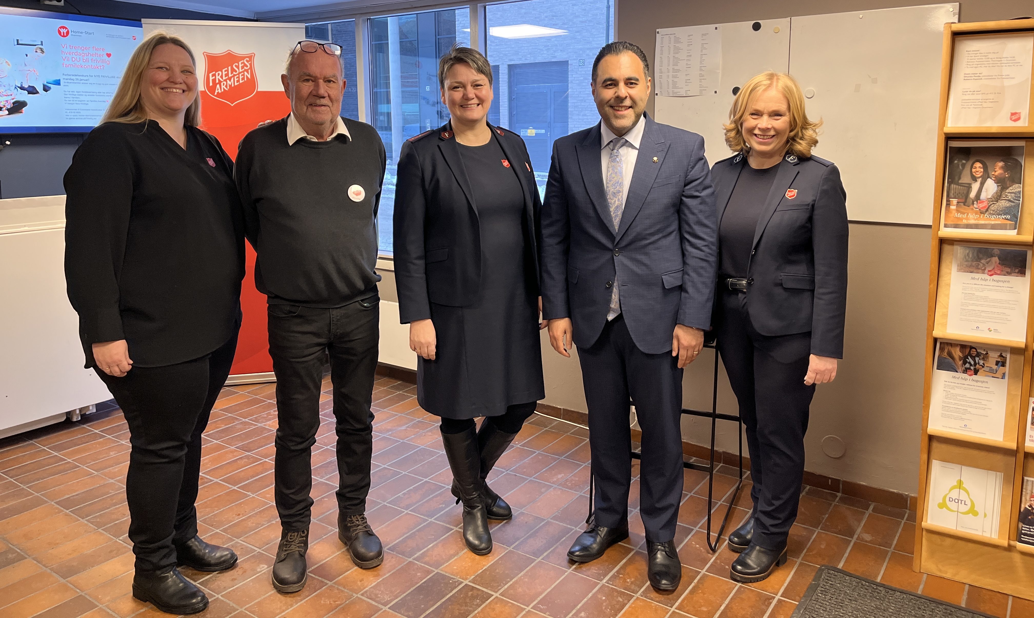 Foto: Tre kvinner og to menn står på rekke i et rom med en logo fra Frelsesarmeen bak på en logo.