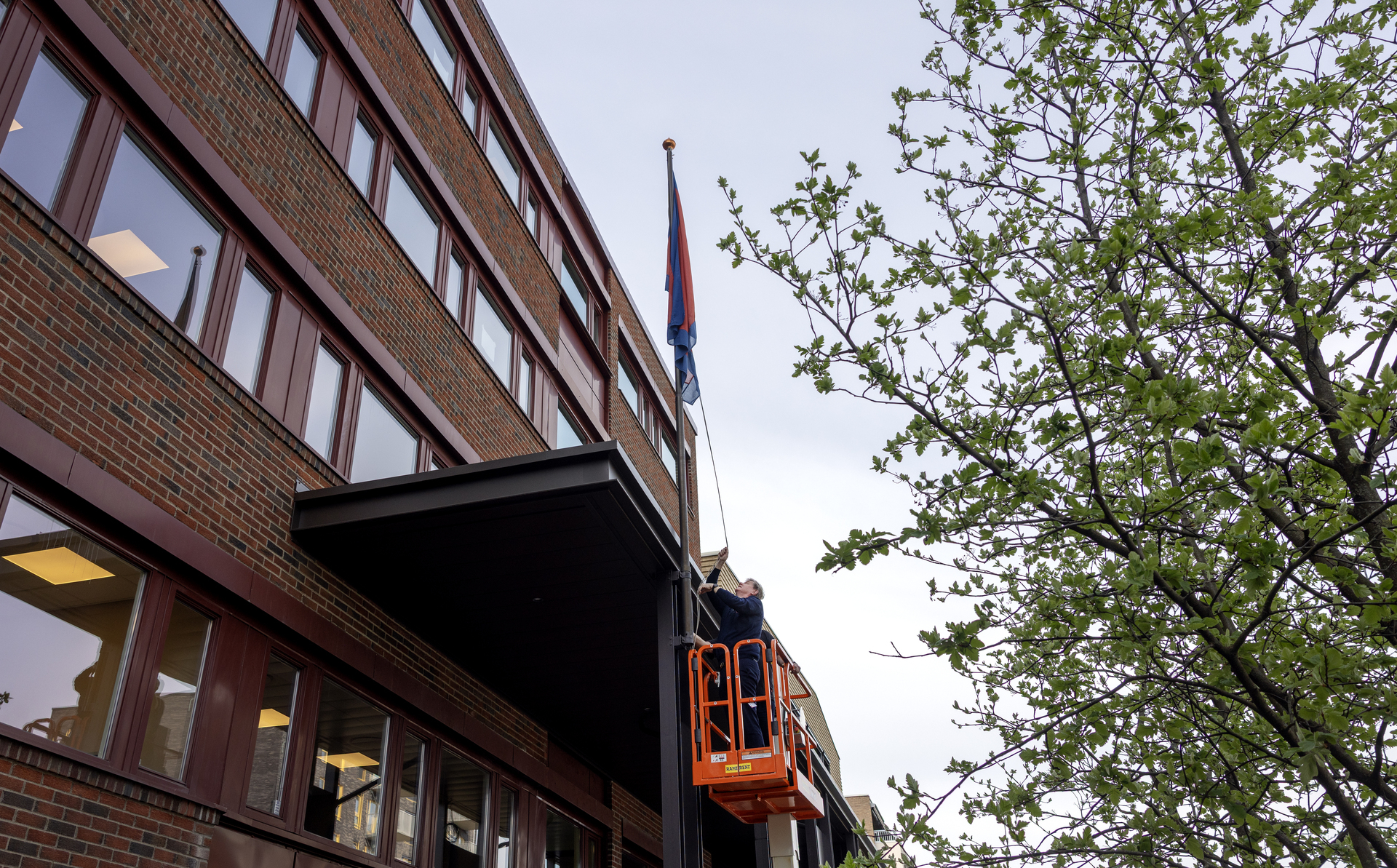 Foto: Mann i 60-årene står i korga til en lift og heiser flagget.