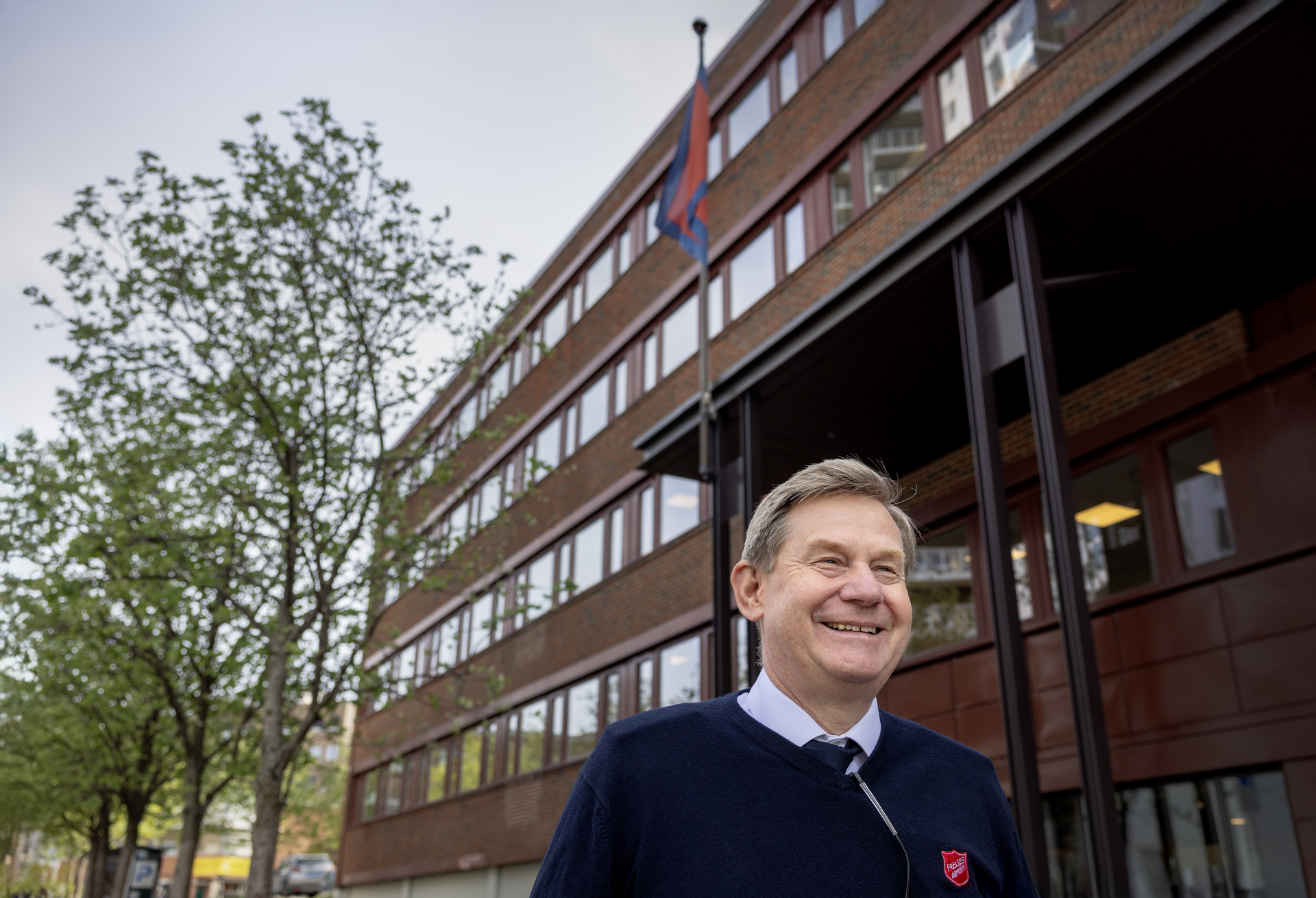 Foto: Mann i 60-årene smiler utenfor bygget mens flagget er til topps.