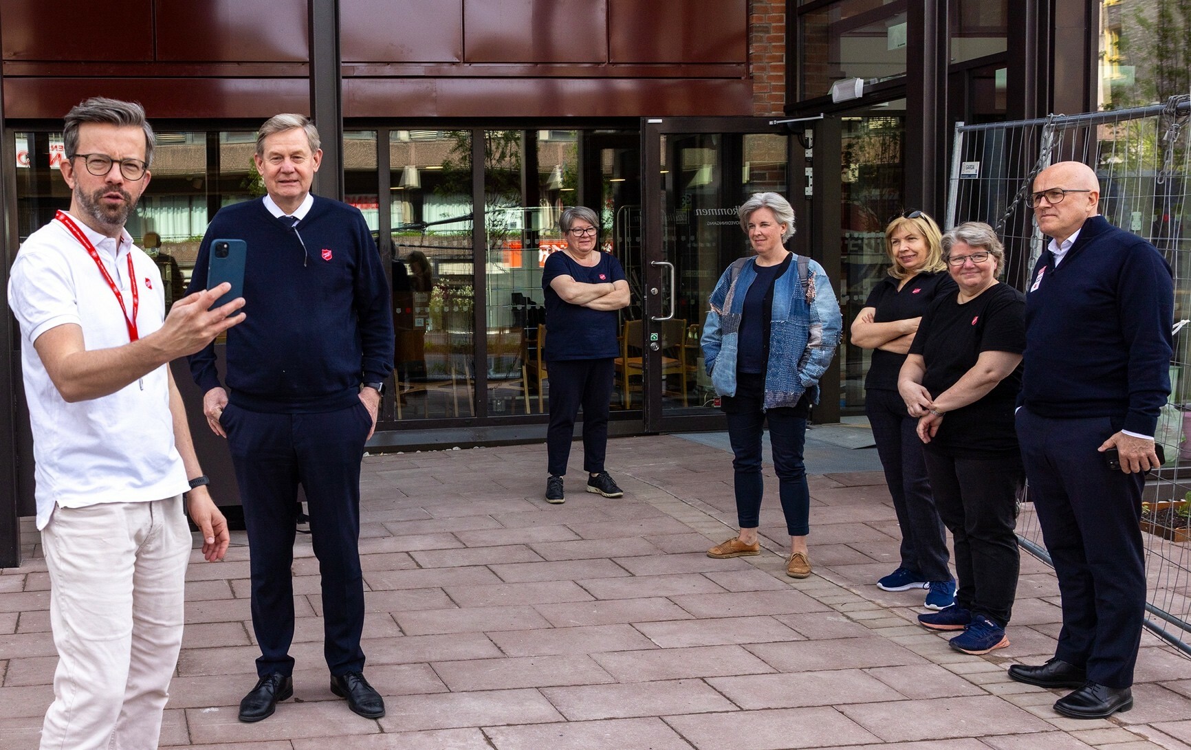 Foto: Mann i 40-årene med briller, hår og skjegg filmer med mobilen. Han har på seg en kortermet, hvit trøye og de som står bak er alle mørkkledde.
