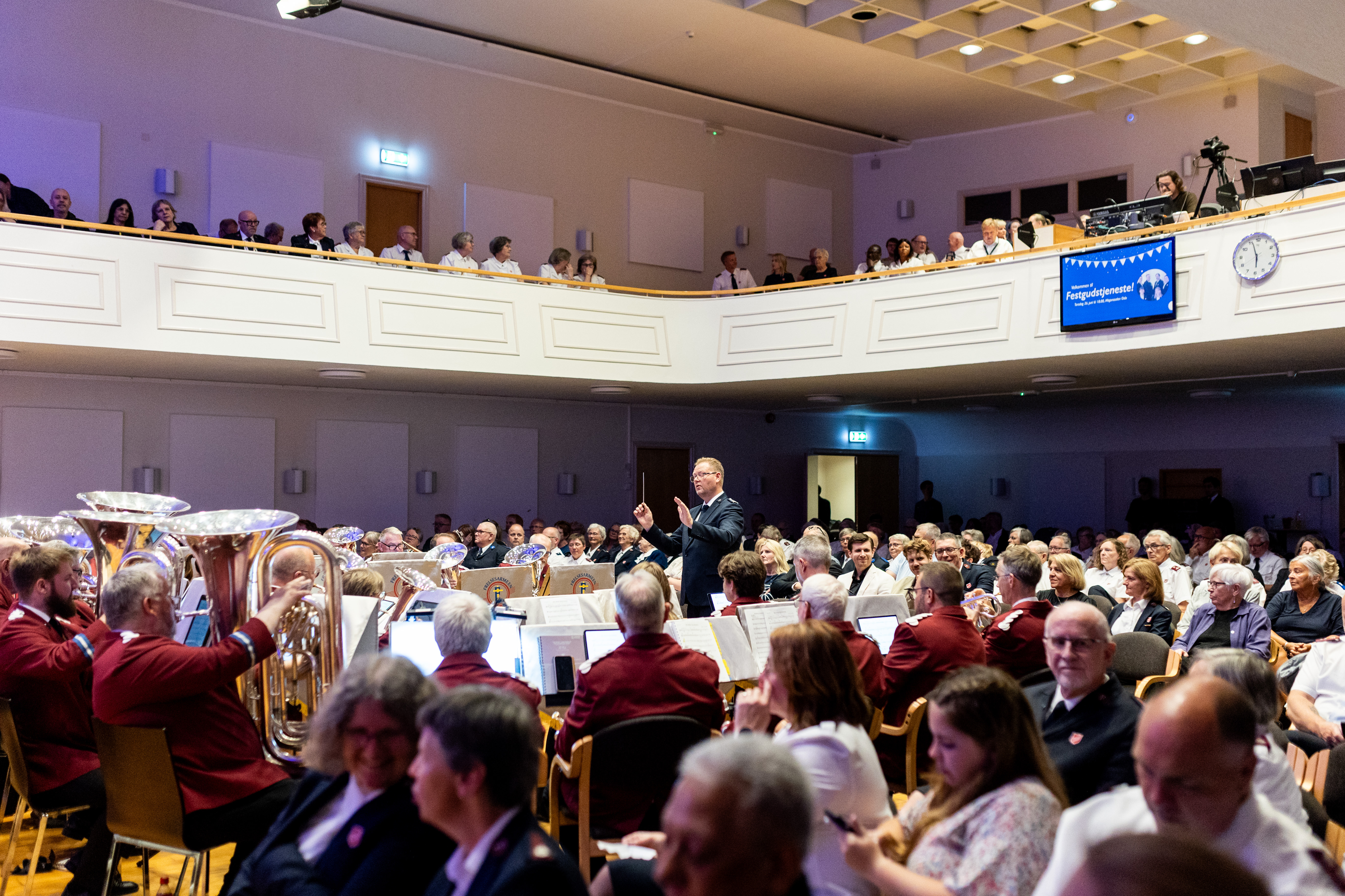 Bilde fra Misjonssalen i Oslo. Det er fullsatt av folk fra Frelsesarmeen. I fokus på bildet set vi et hornorkster spille.
